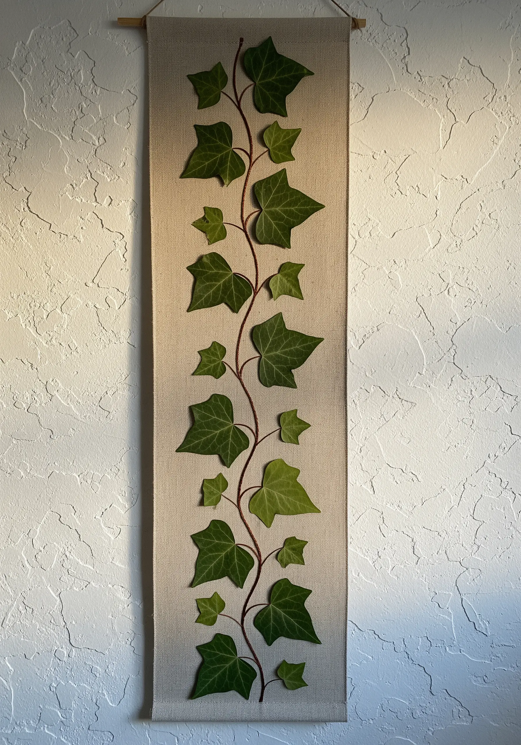 A climbing vine of pressed ivy and embroidery on a fabric wall hanging.