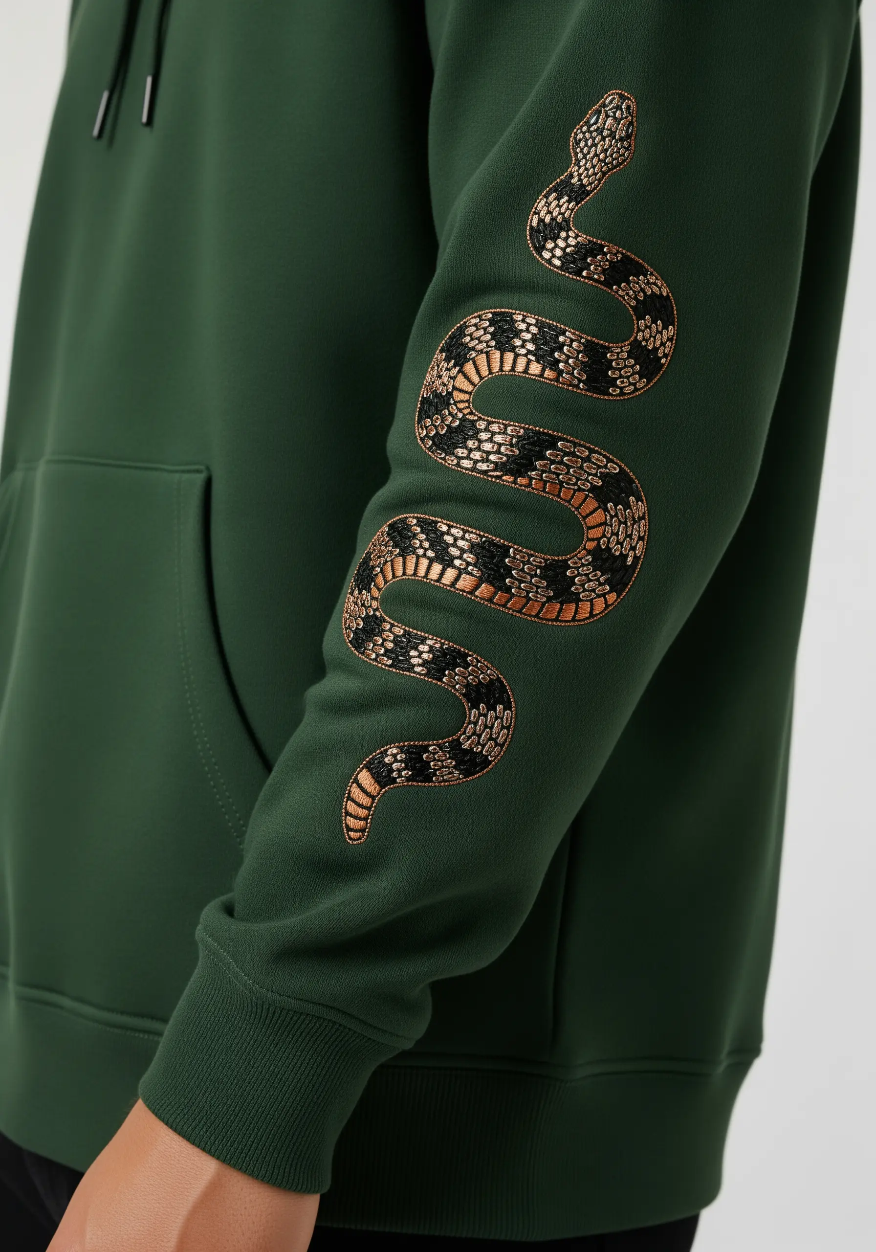 A detailed snake with gold and black scales embroidered along the sleeve of a green hoodie.