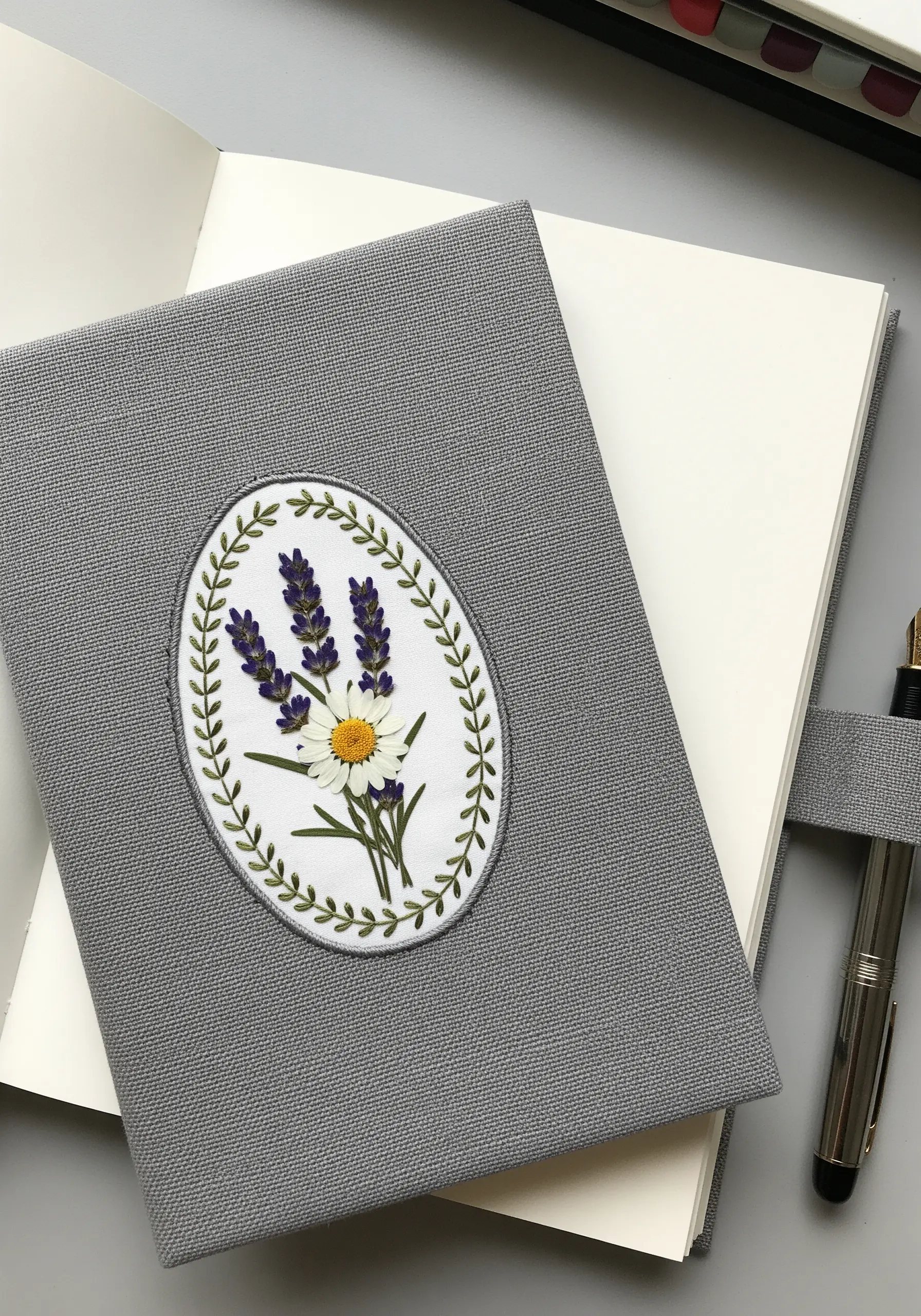 An embroidered patch with pressed lavender and a daisy, placed on a grey journal cover.