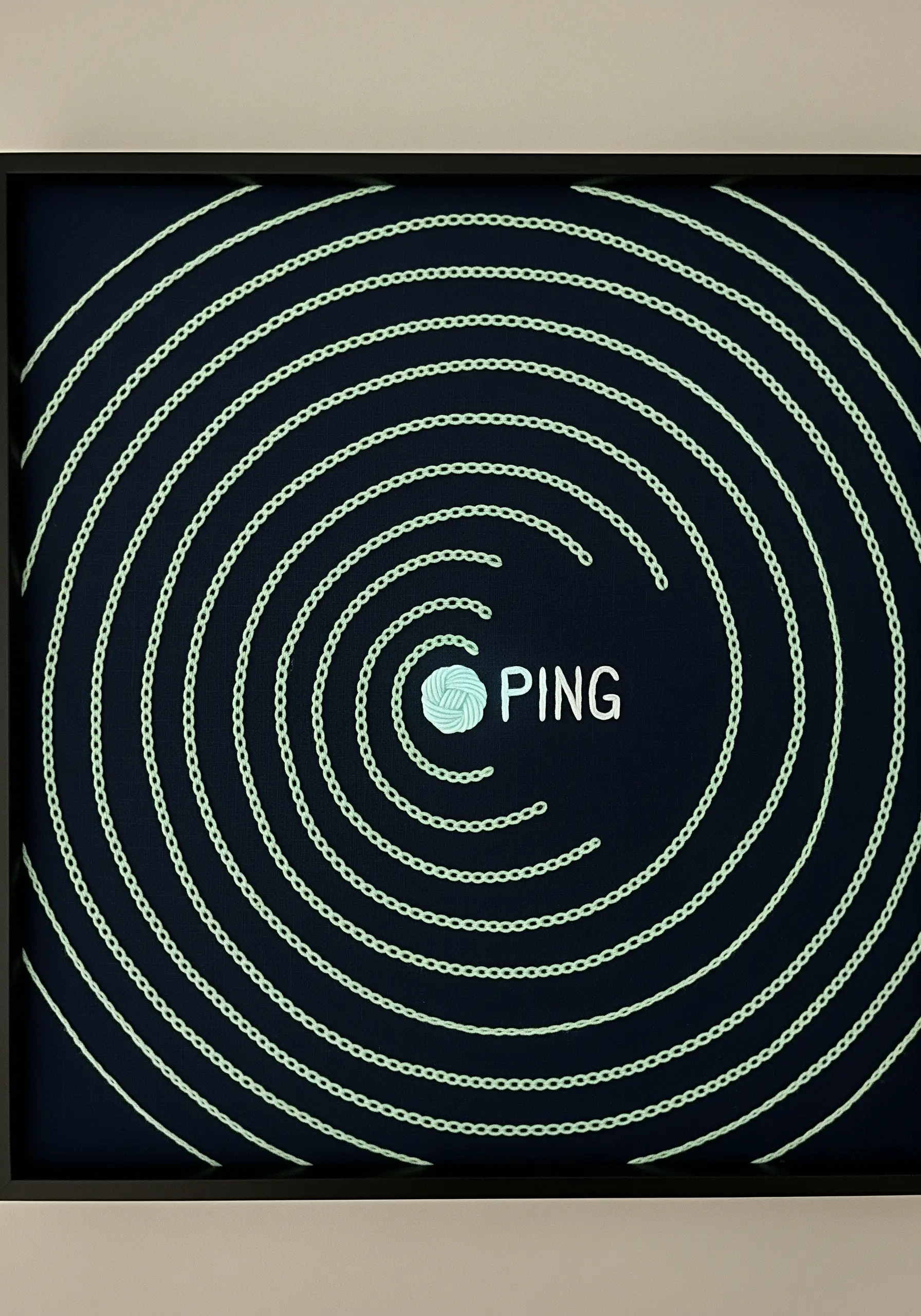 A digital 'ping' embroidered with concentric chain stitches in light green on a dark background.