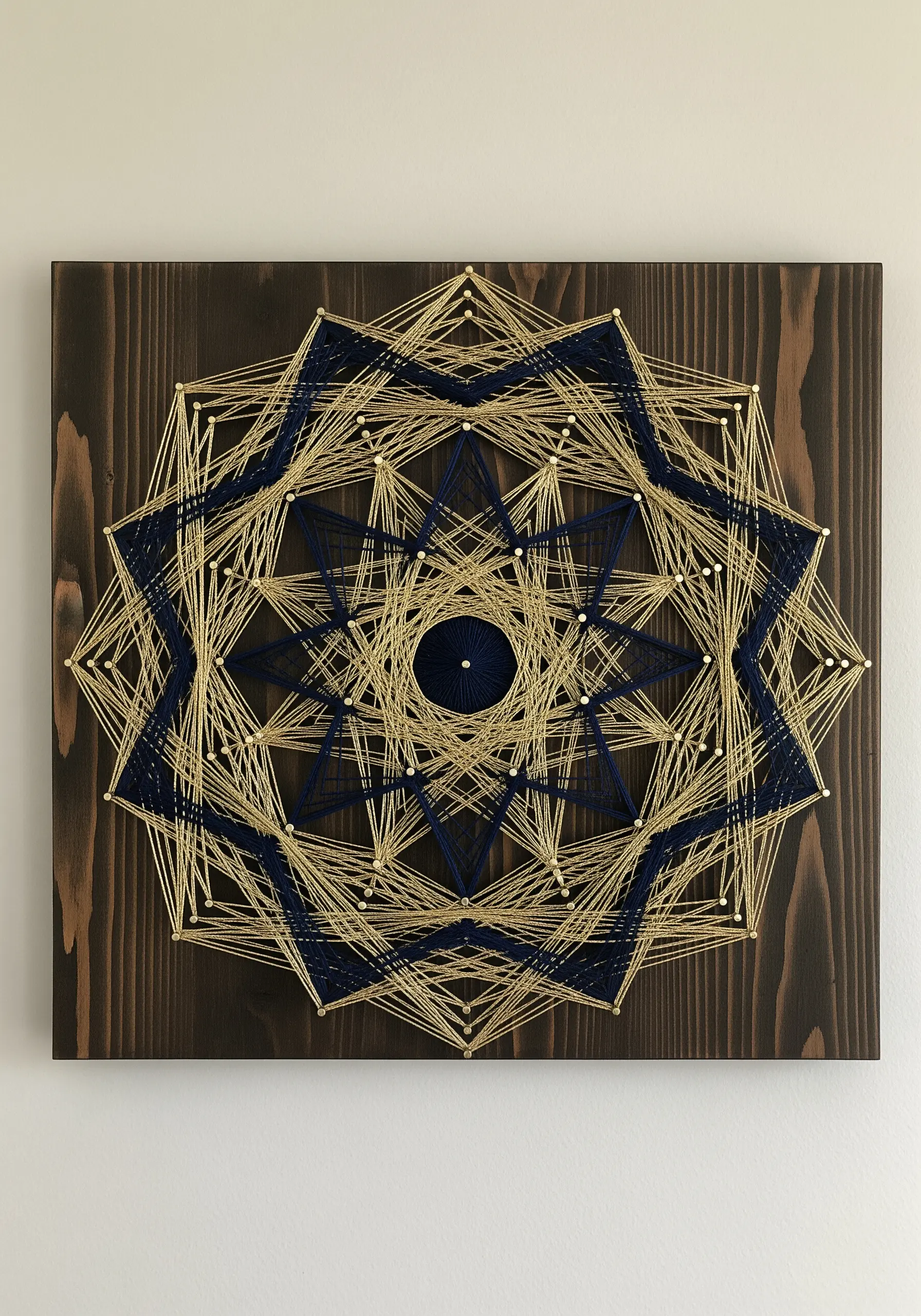 Geometric string art mandala with blue and gold thread on a dark wood board.