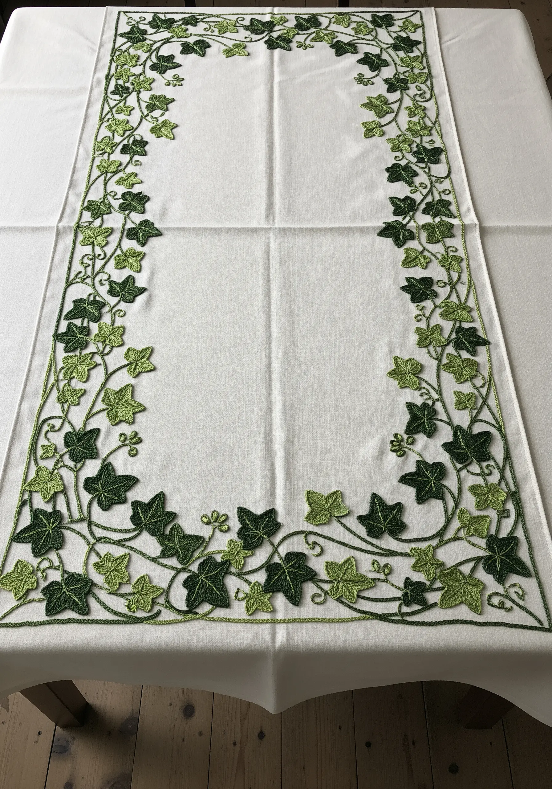 A white tablecloth with a dense, winding border of ivy leaves in two shades of green.
