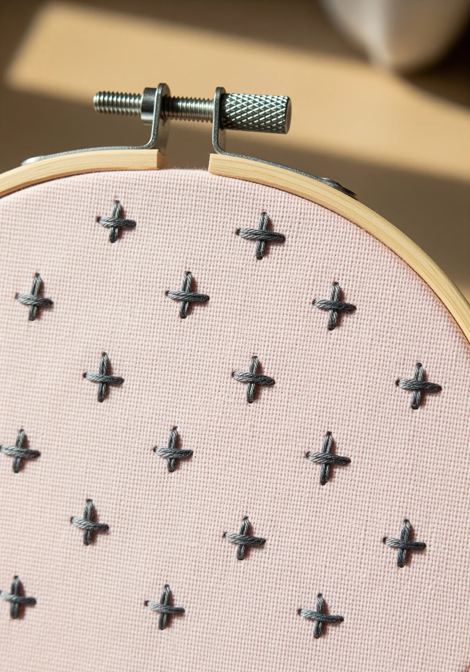A grid pattern of simple gray cross stitches on pink fabric.