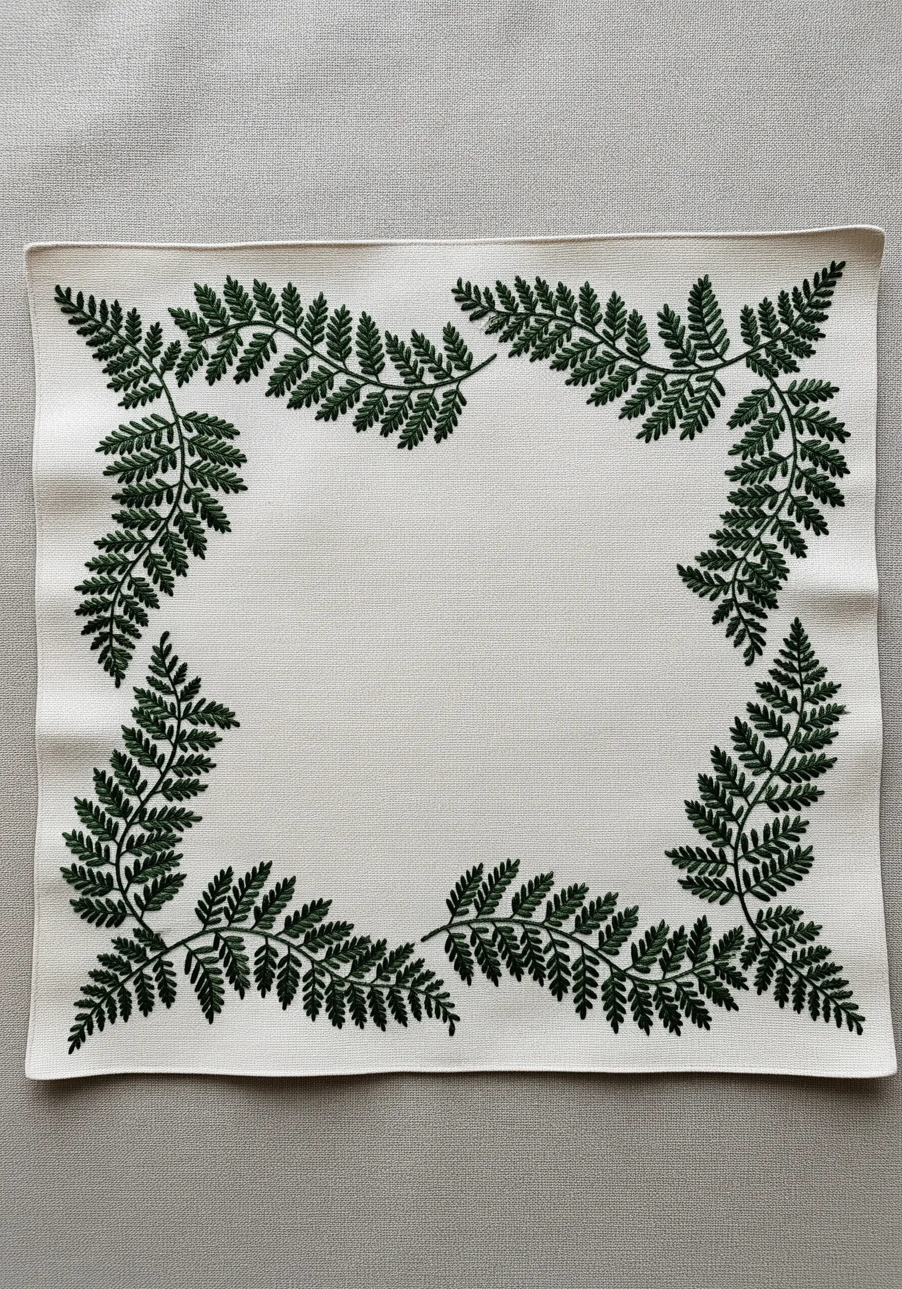 A rectangular placemat with a dense, dark green fern border embroidered in a single color.