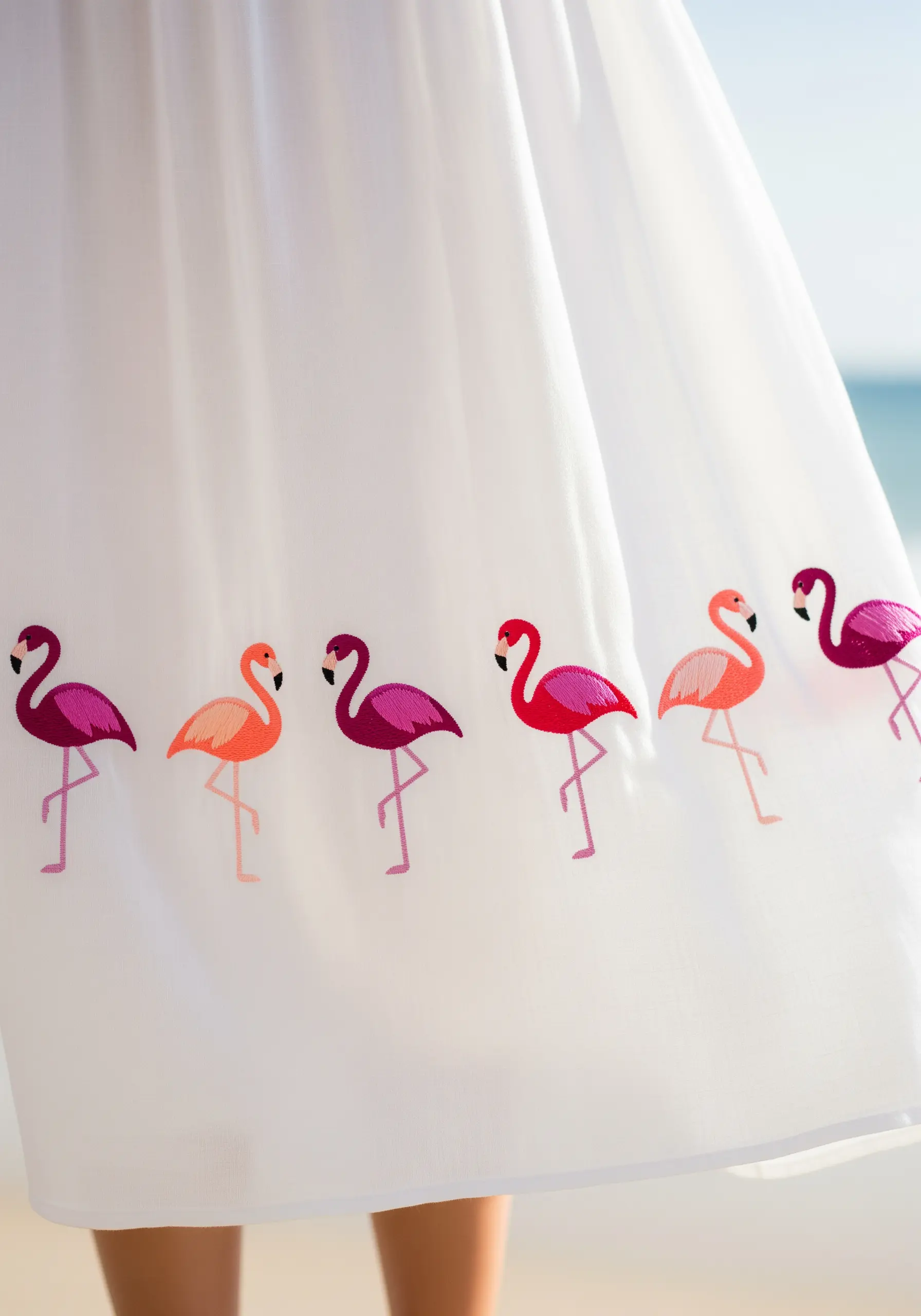 A row of colorful satin-stitched flamingos marching along the hem of a white skirt.