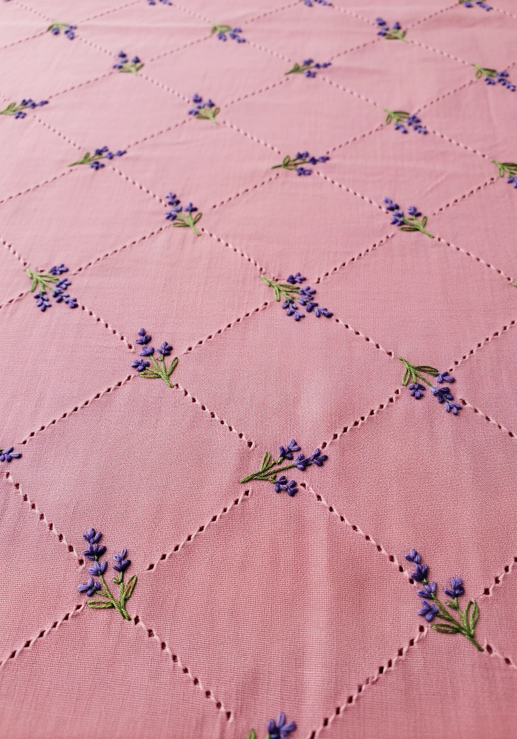 A pink tablecloth with a diamond grid of decorative stitching and tiny lavender sprigs.