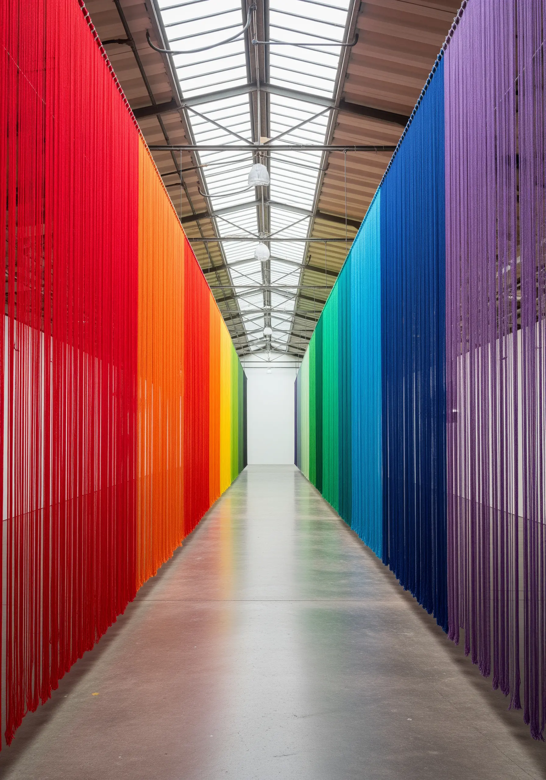 A long corridor lined with floor-to-ceiling strands of yarn in a perfect rainbow gradient.