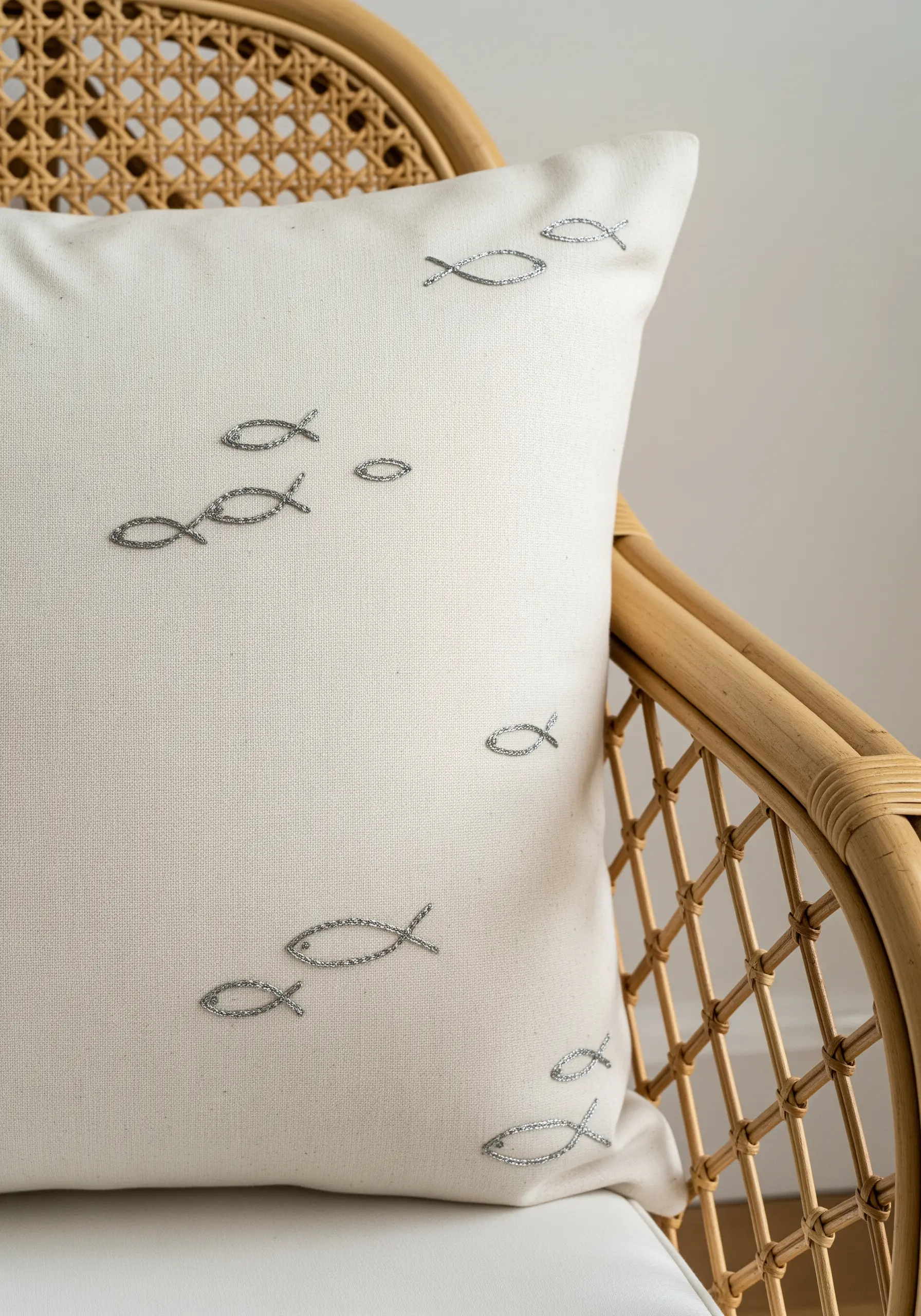 A white pillow cover decorated with a scattered pattern of small, silver embroidered fish.