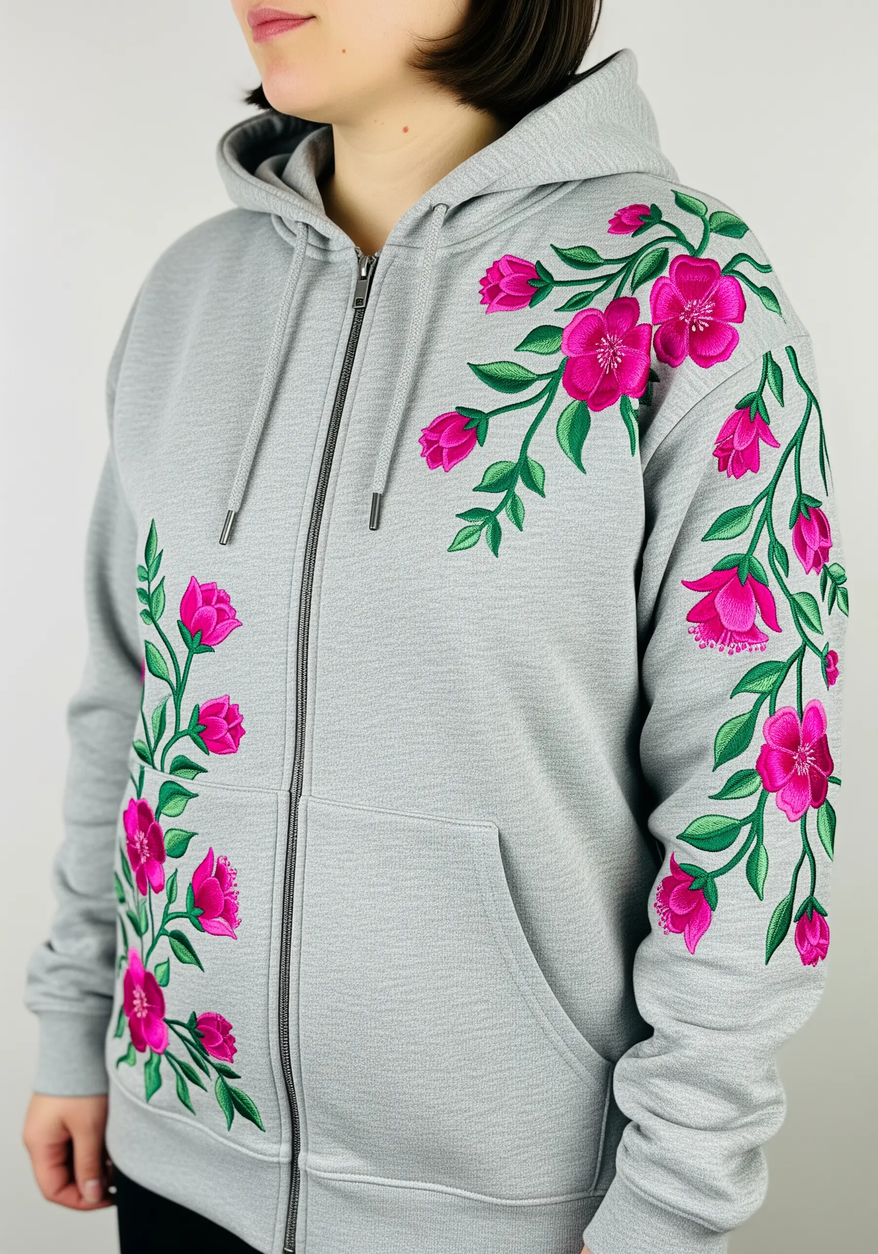 Bright pink floral vines embroidered asymmetrically on the front of a grey zip-up hoodie.