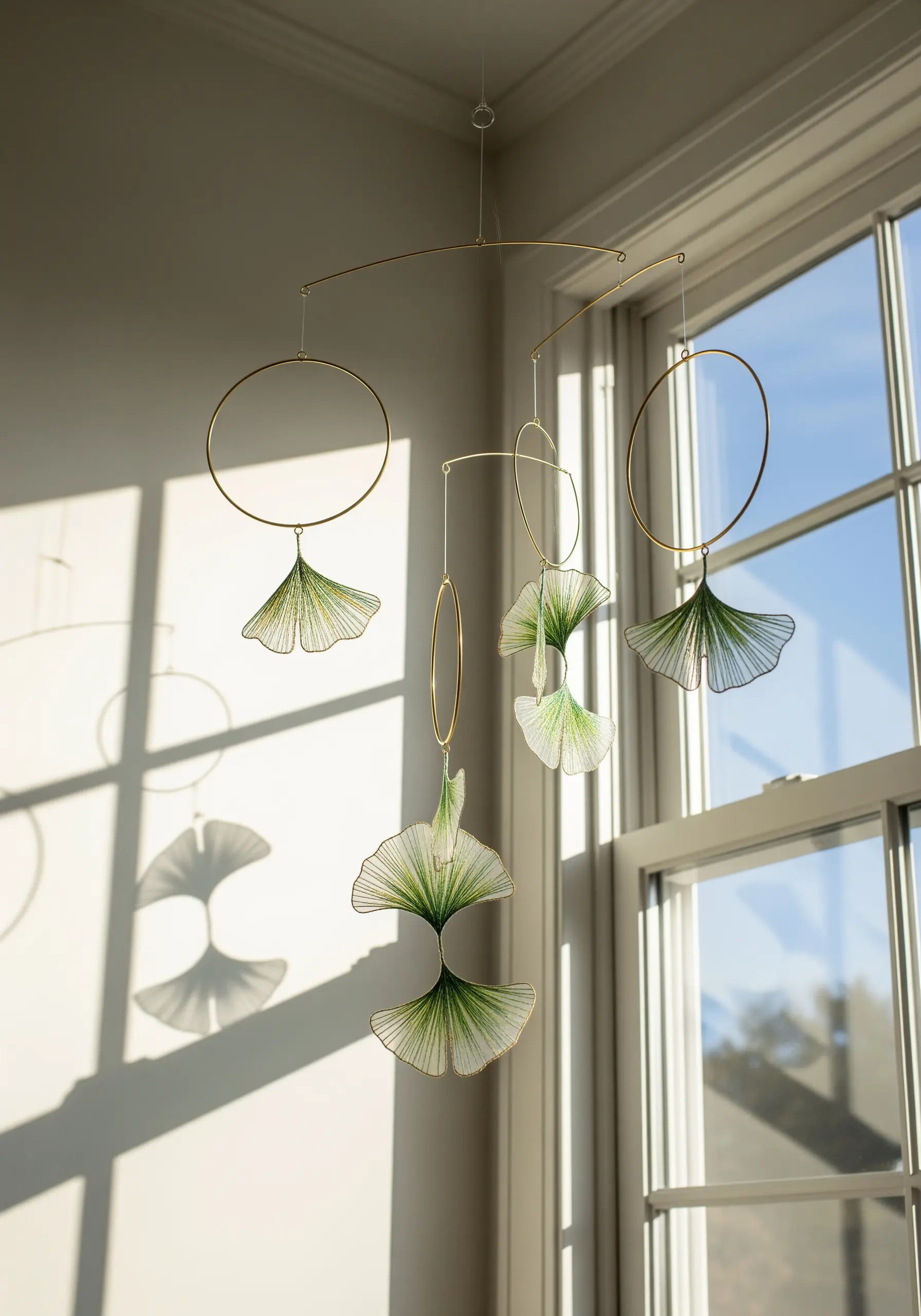 A delicate mobile with green thread creating ginkgo leaf shapes within gold metal frames.