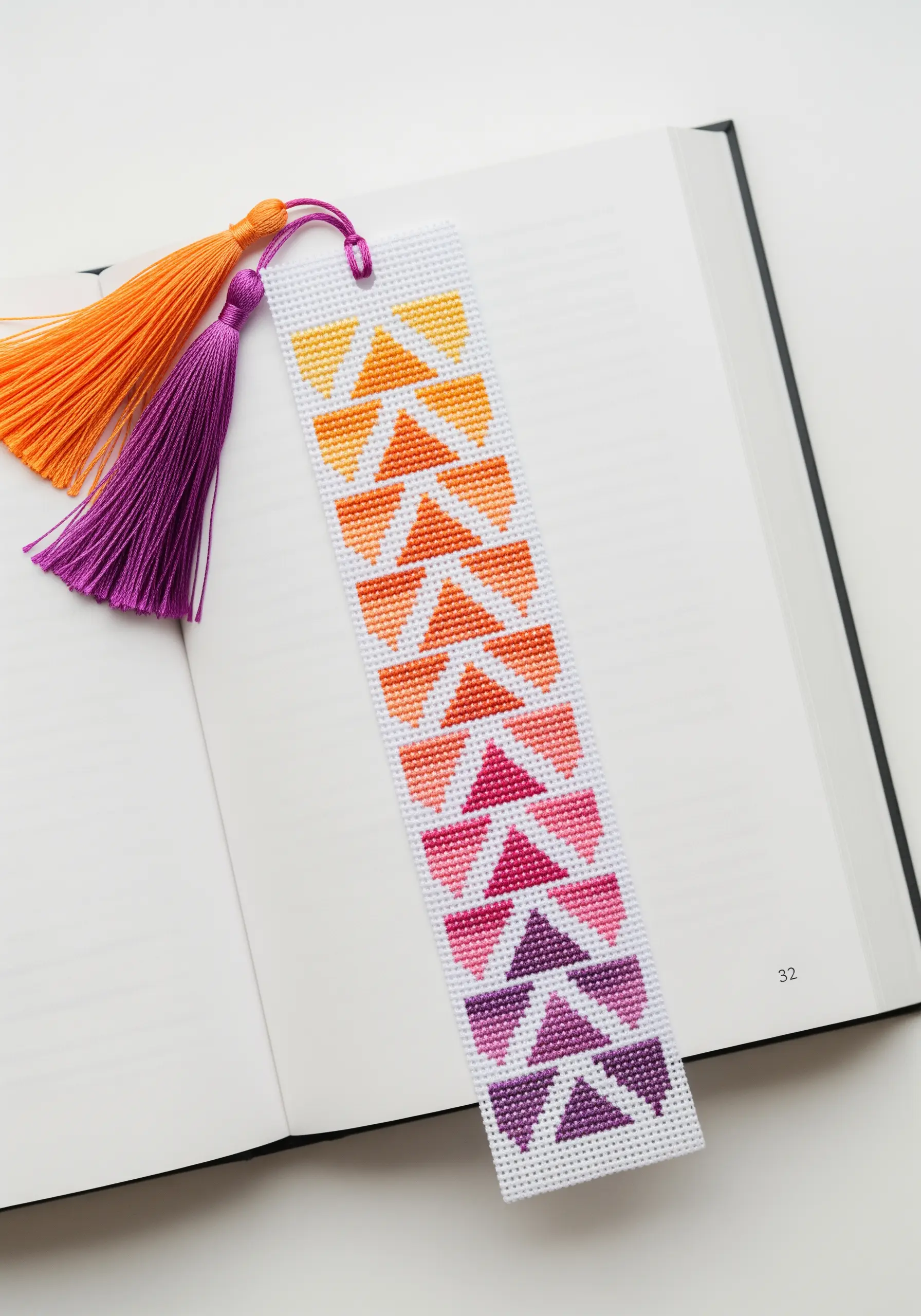 A cross-stitch bookmark with a geometric pattern in a warm color gradient.