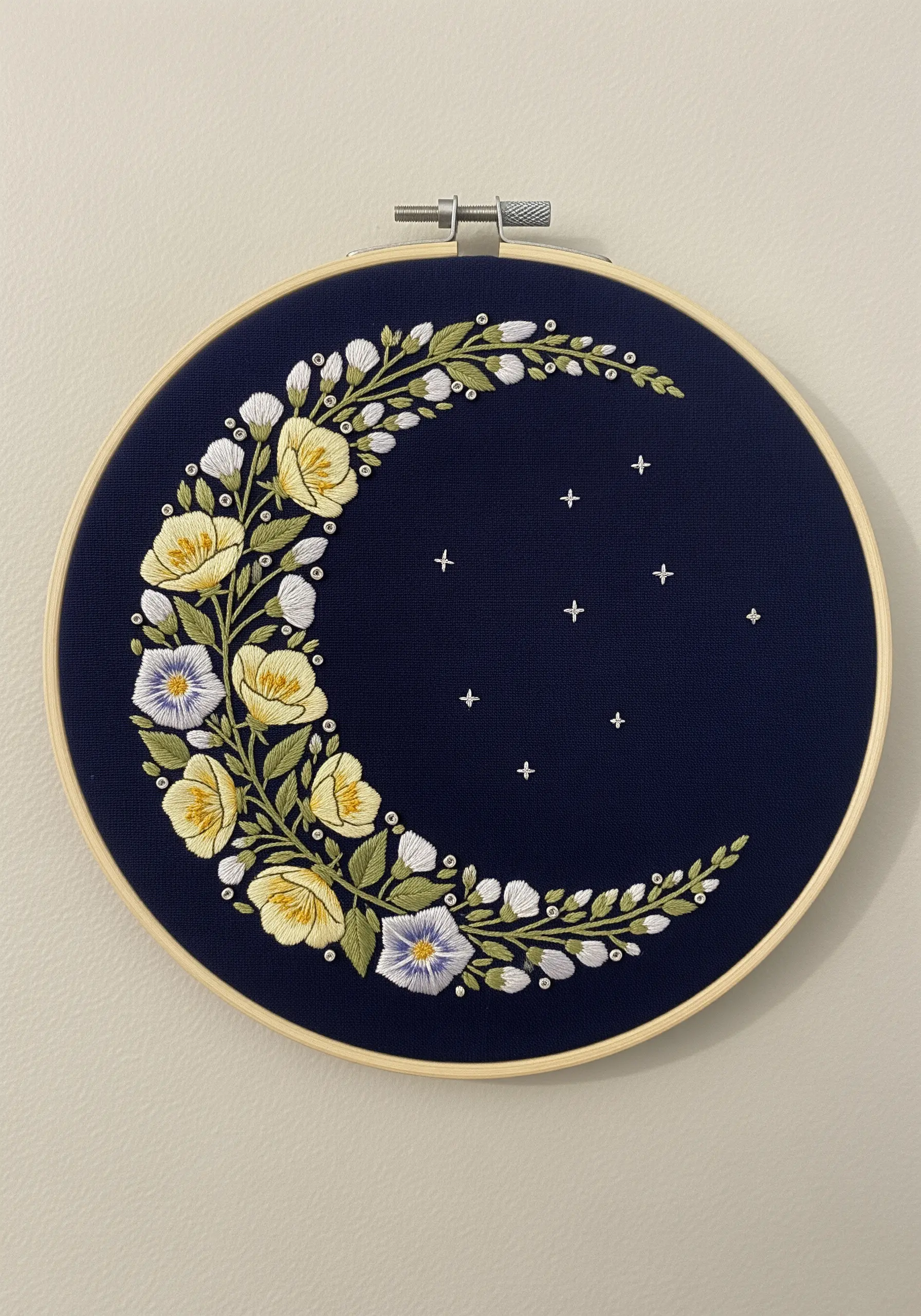 A crescent moon shape filled with an arrangement of yellow, white, and purple embroidered flowers.