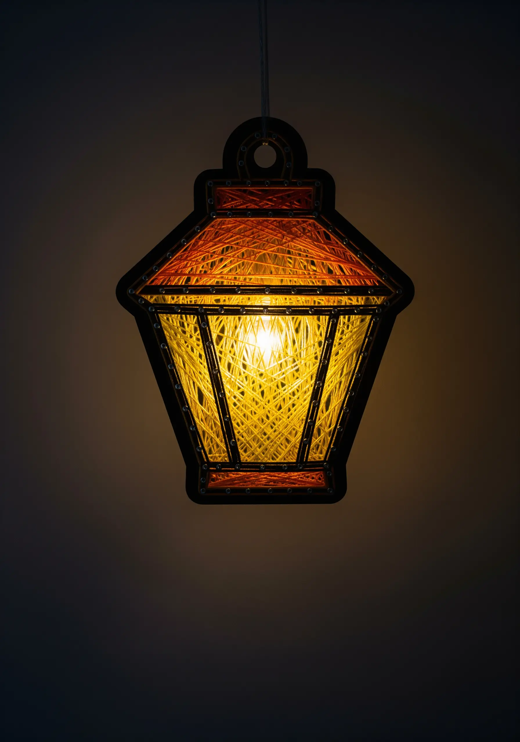 A string art lantern with orange and yellow threads, illuminated from within.