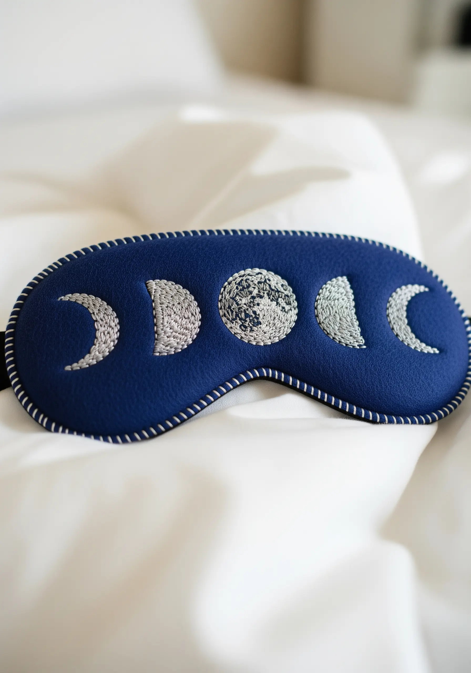 A blue sleep mask embroidered with the phases of the moon in silver thread