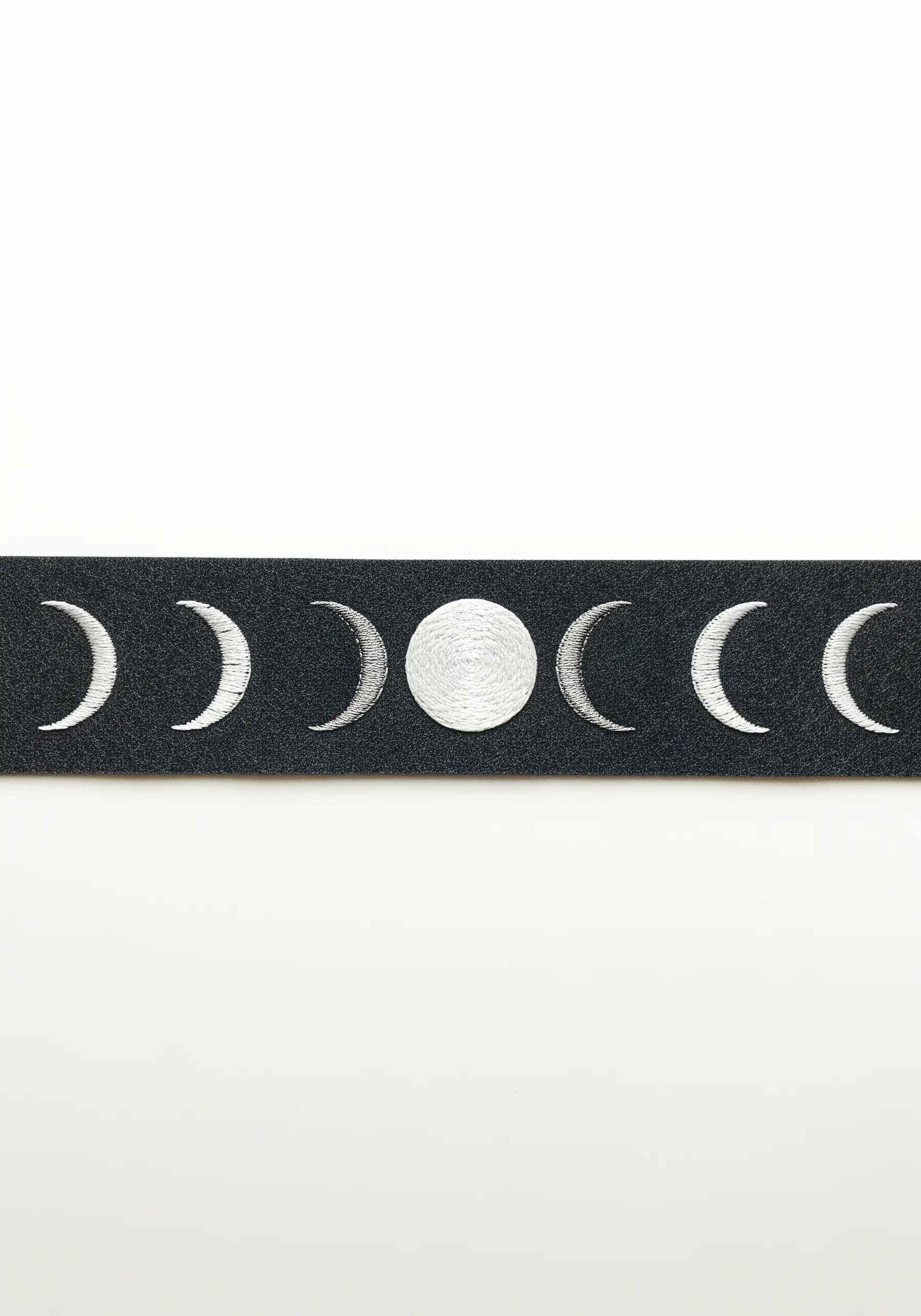 A linear embroidery of the phases of the moon in silver and gray thread on black fabric.