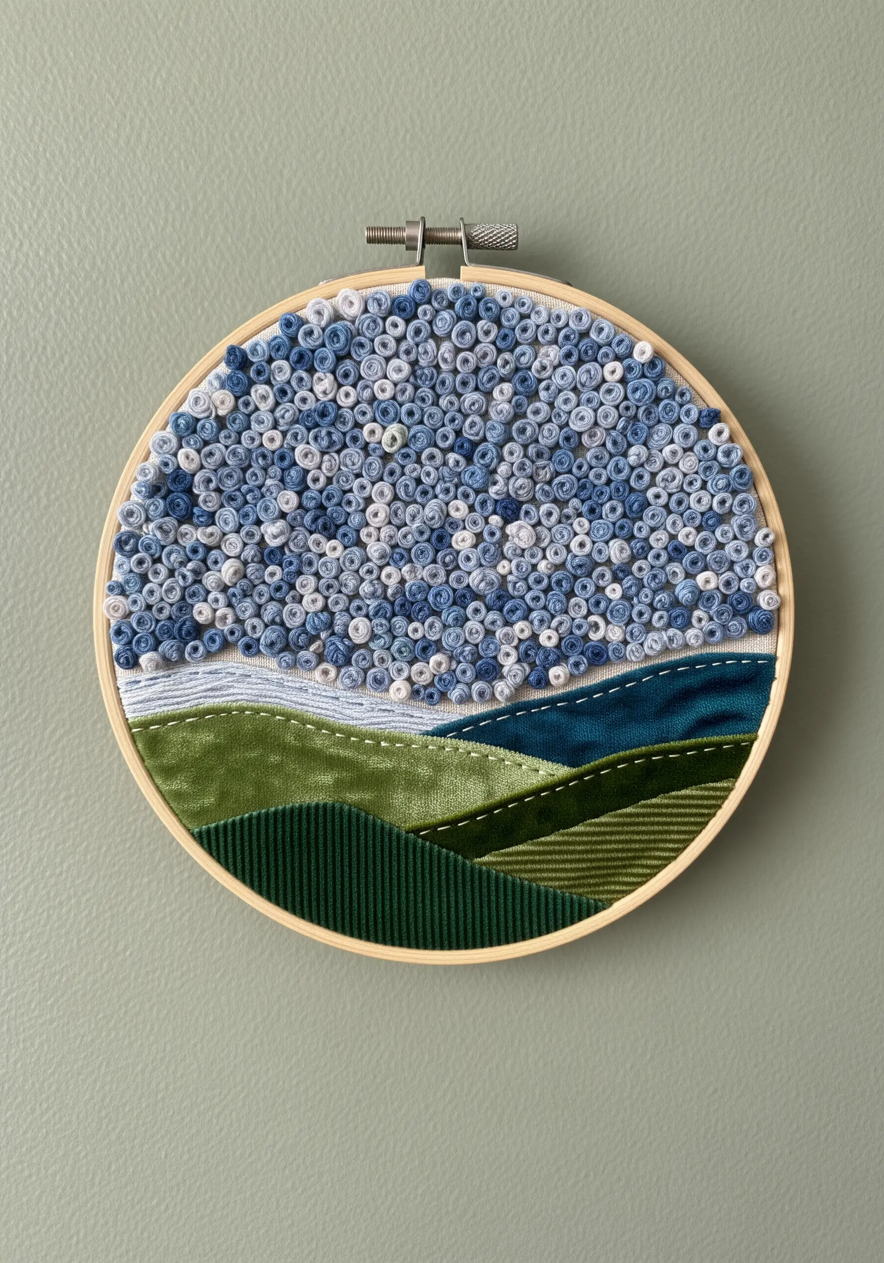 Embroidery hoop art of a landscape with fabric hills and a sky of blue French knots.