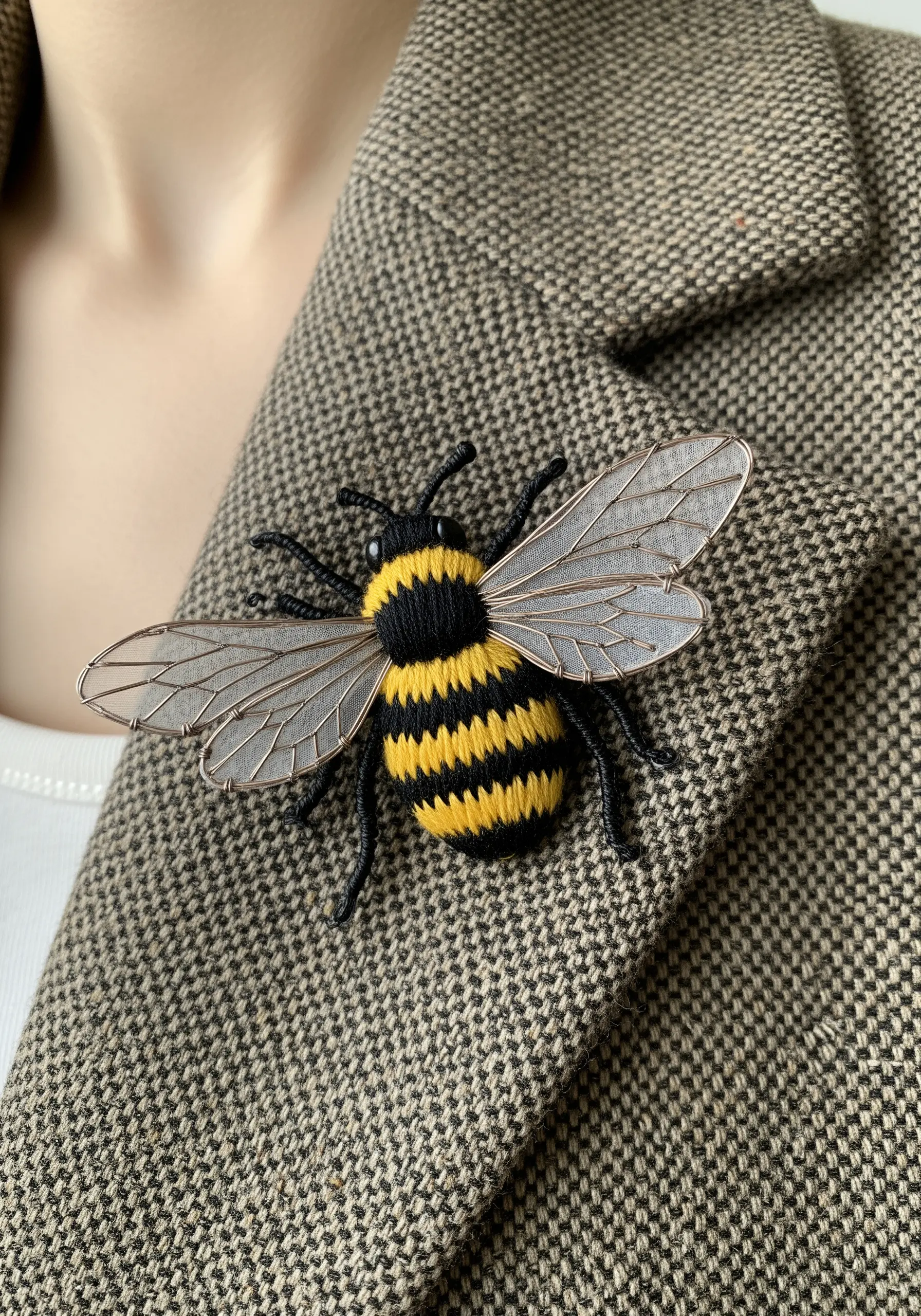 A realistic, three-dimensional embroidered bee brooch pinned to a tweed jacket.