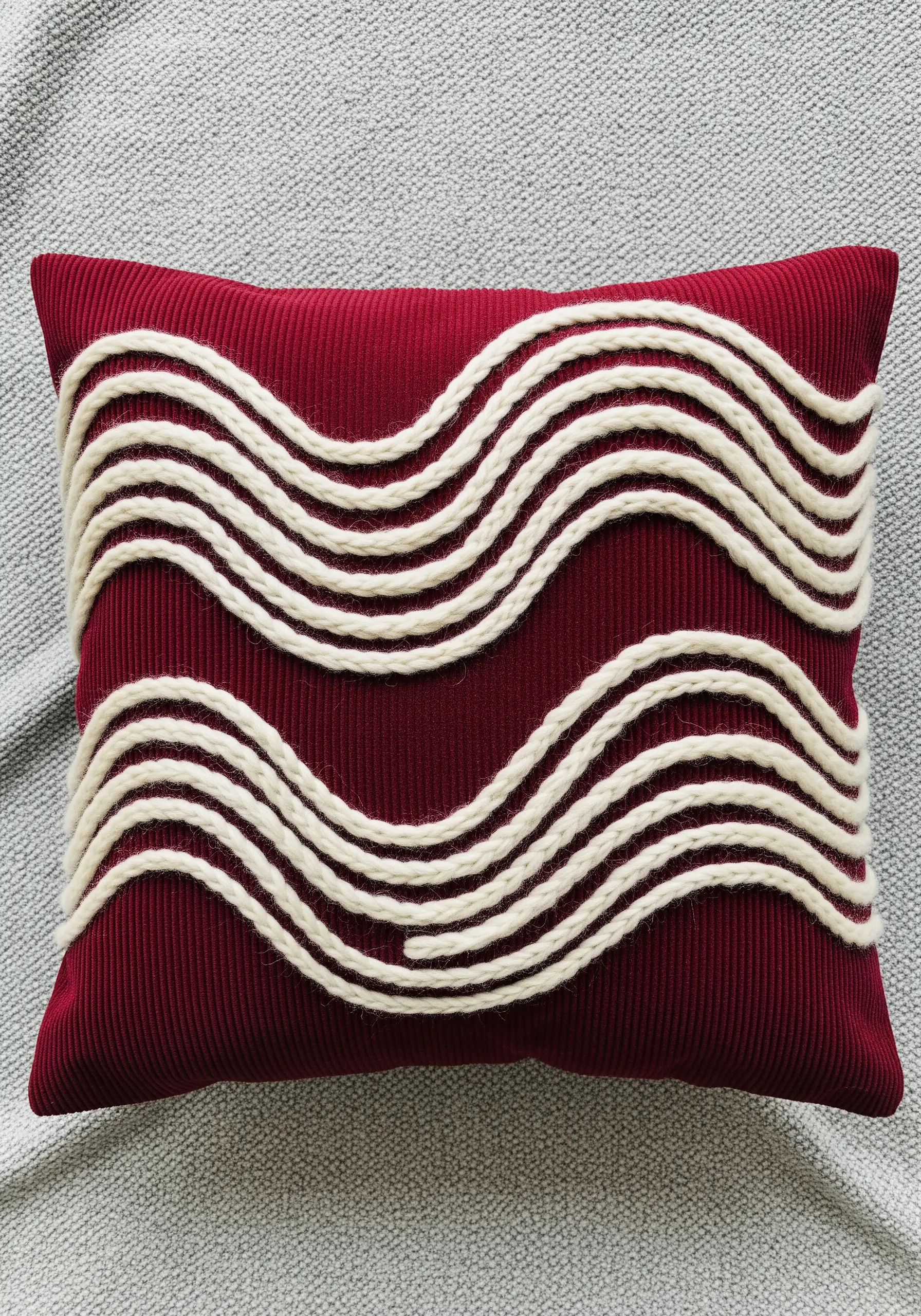 Thick, white yarn couched in wavy lines across a rich red corduroy pillow.