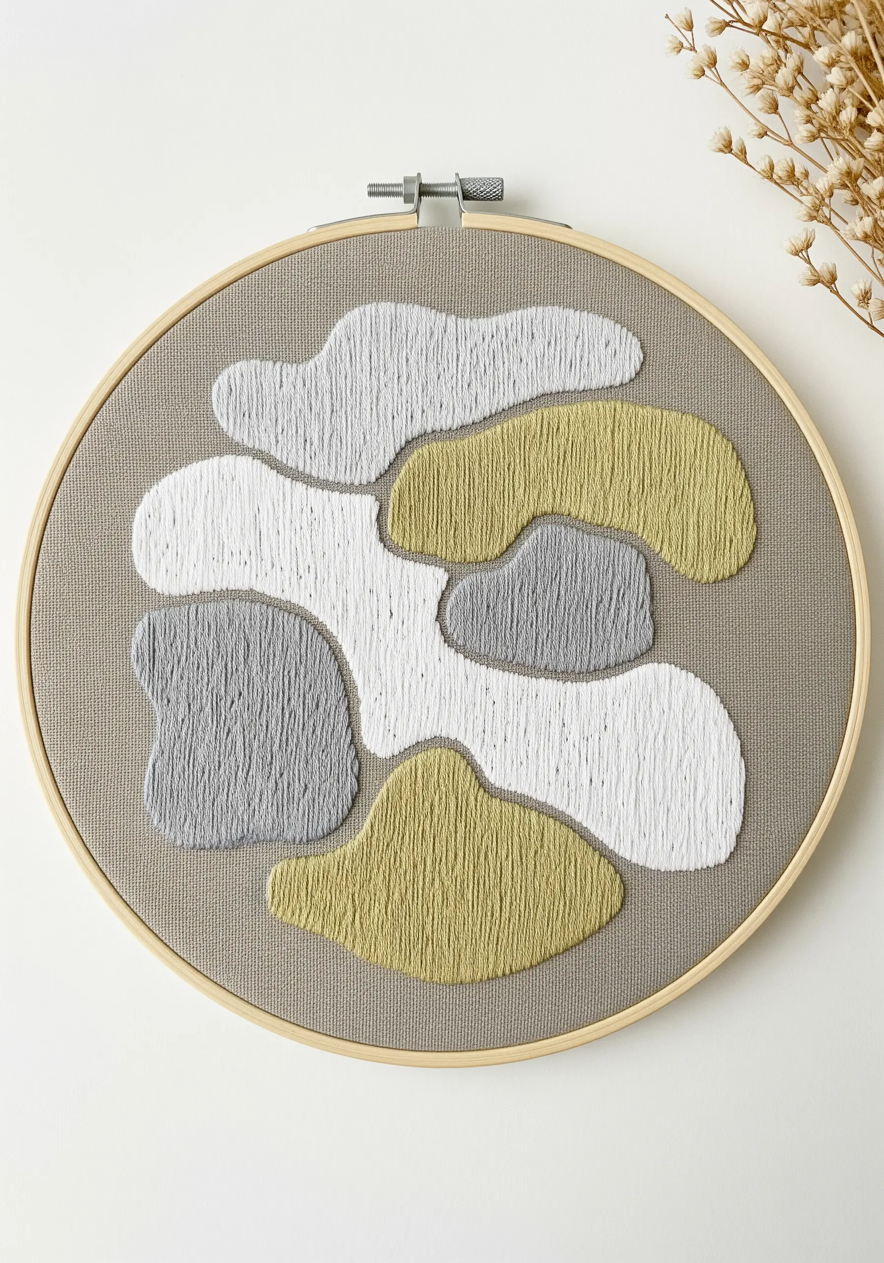Abstract embroidery with organic shapes filled with satin stitch in muted white, gray, and ochre.