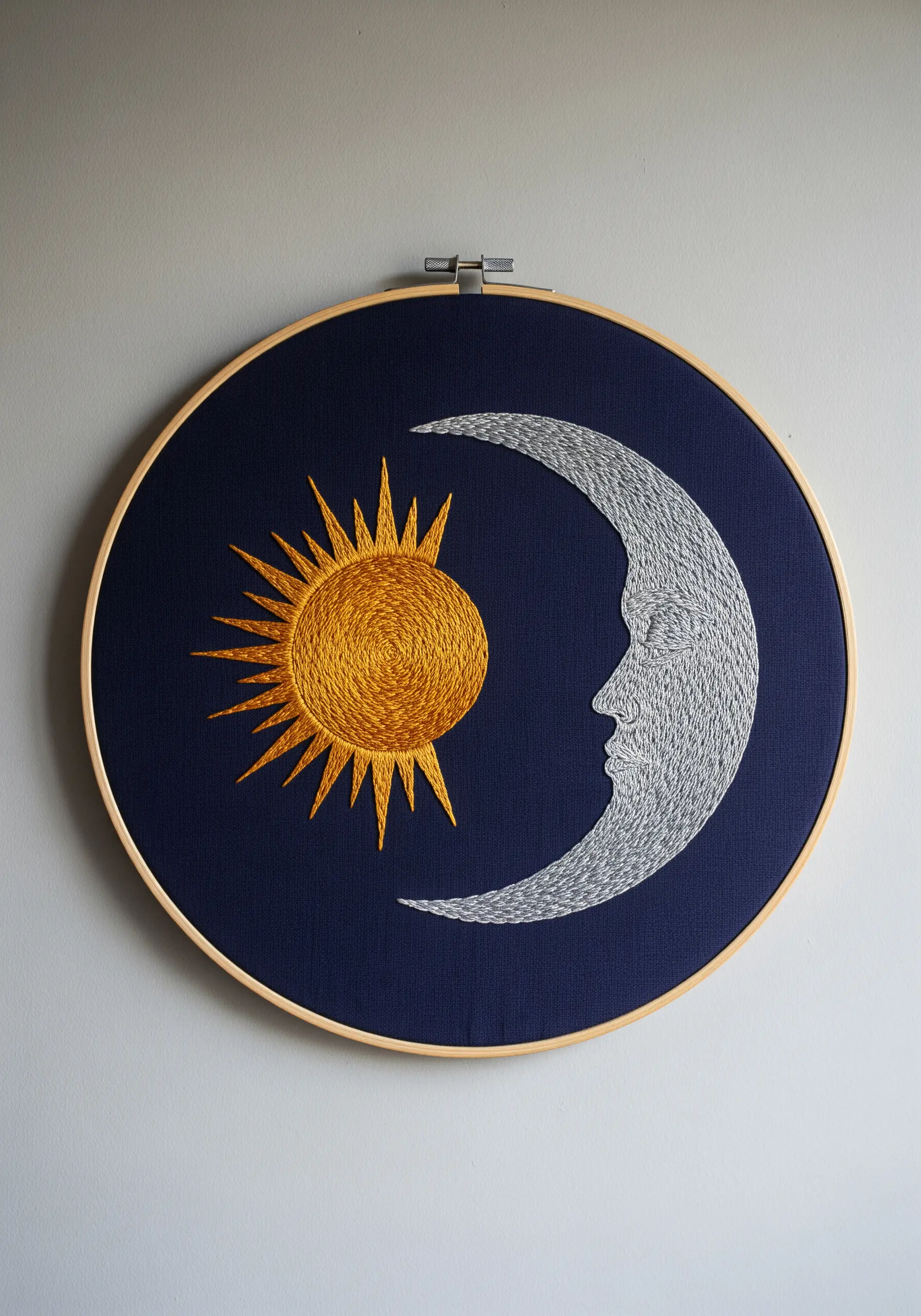 Embroidery hoop with a metallic gold sun and silver moon on a dark blue background.