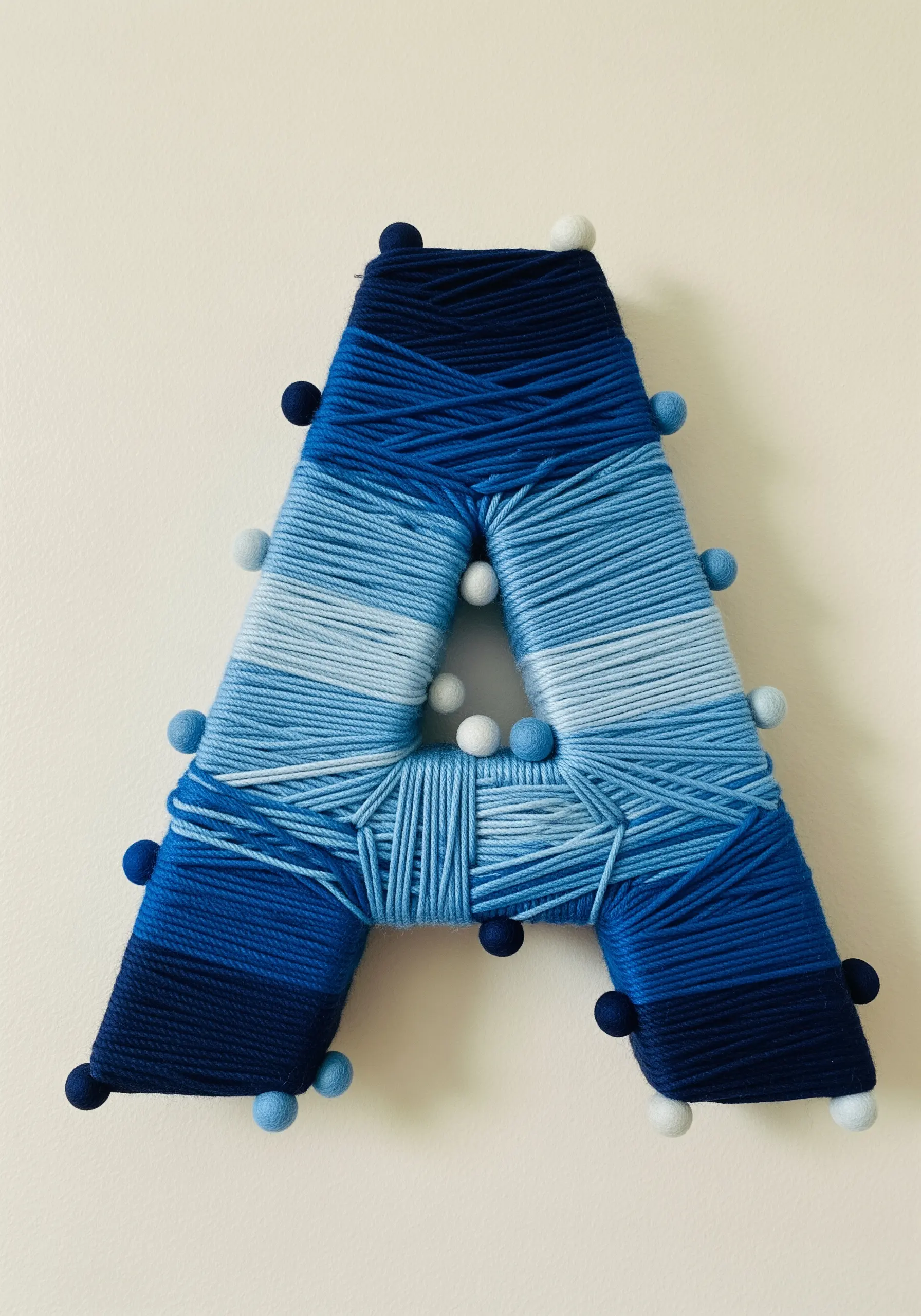 Letter A wrapped in blue ombre yarn with pom-pom accents