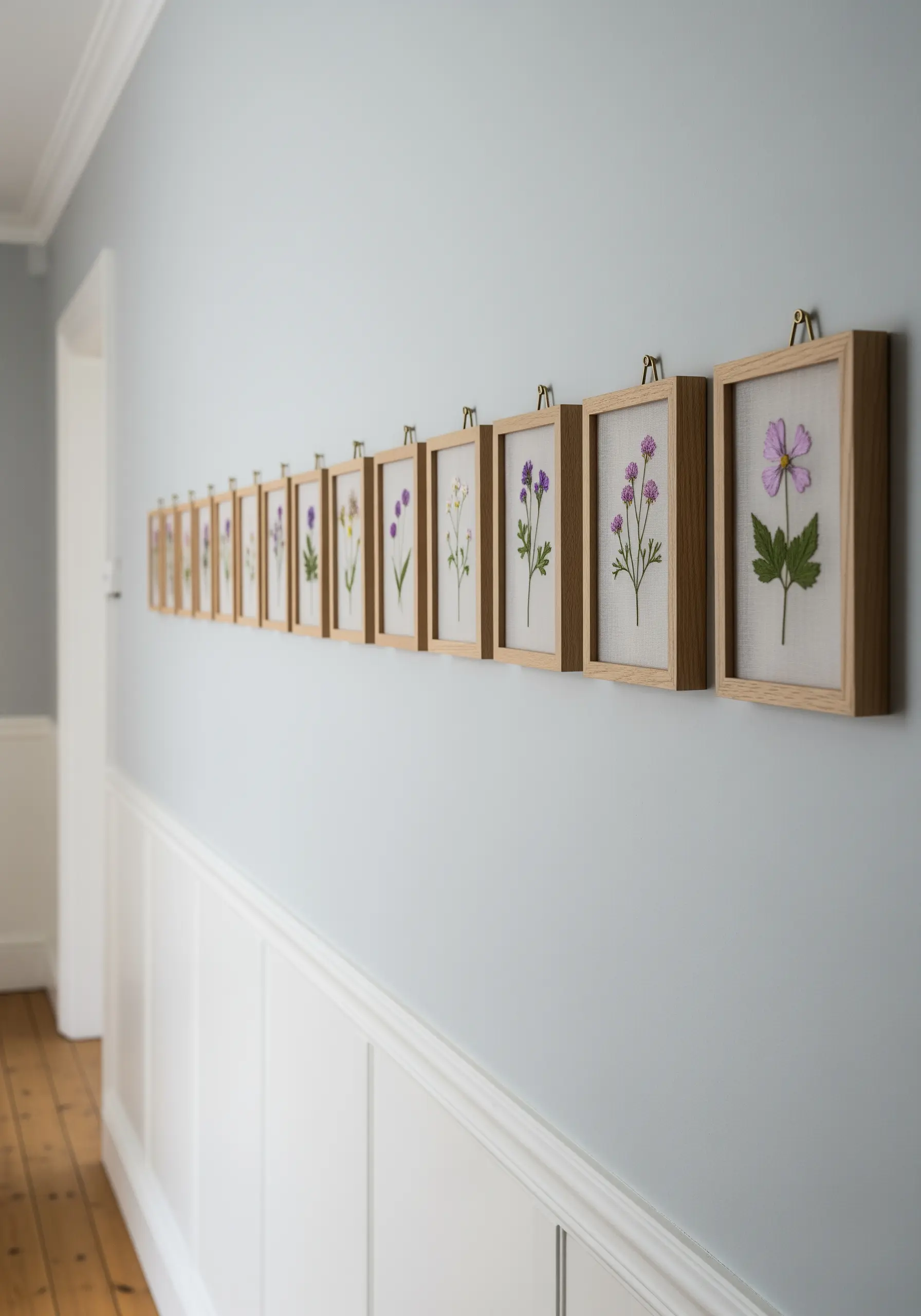A long row of small, individually framed embroidered wildflowers on a light gray wall.