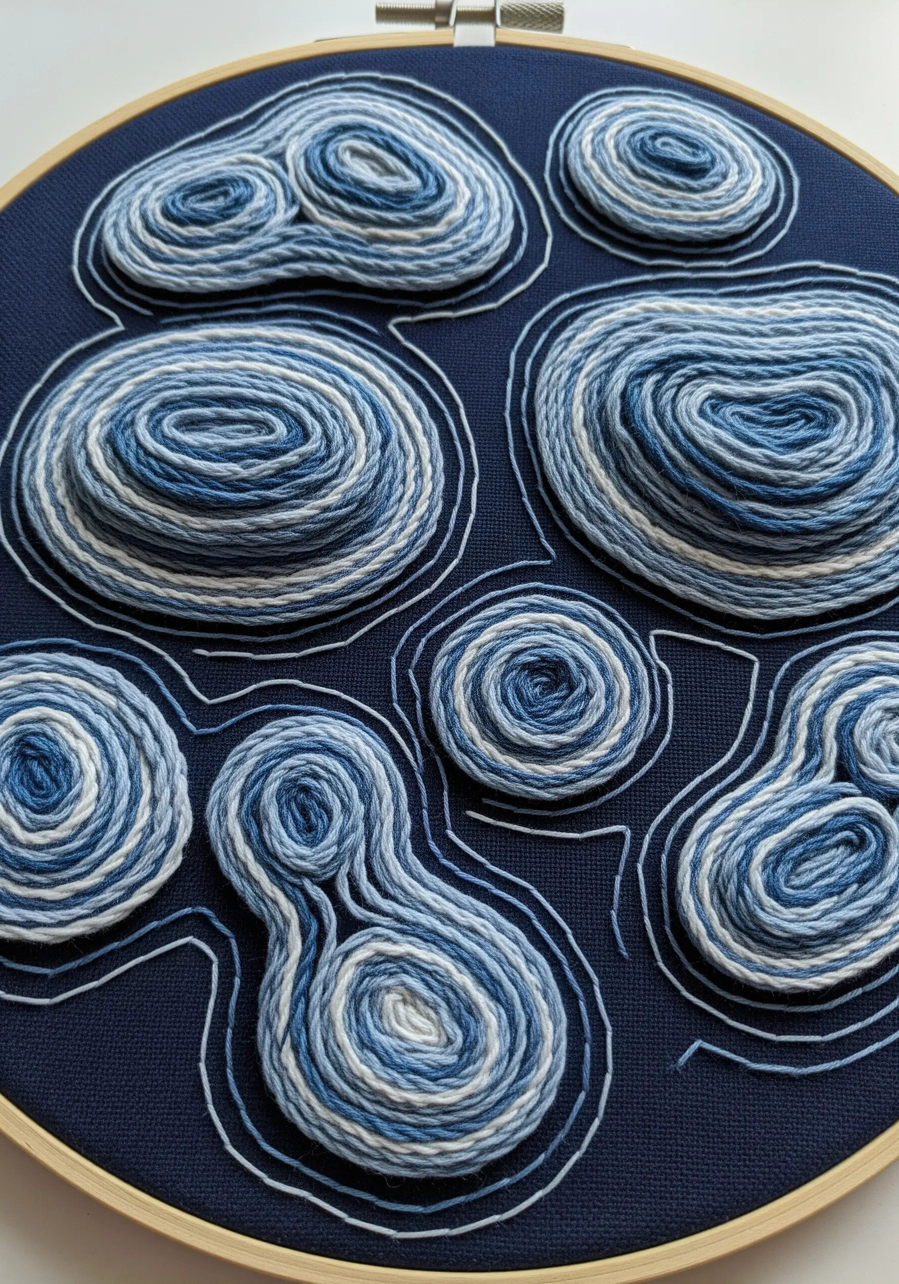 Abstract, swirling shapes created by couching variegated blue and white yarn onto dark blue fabric.