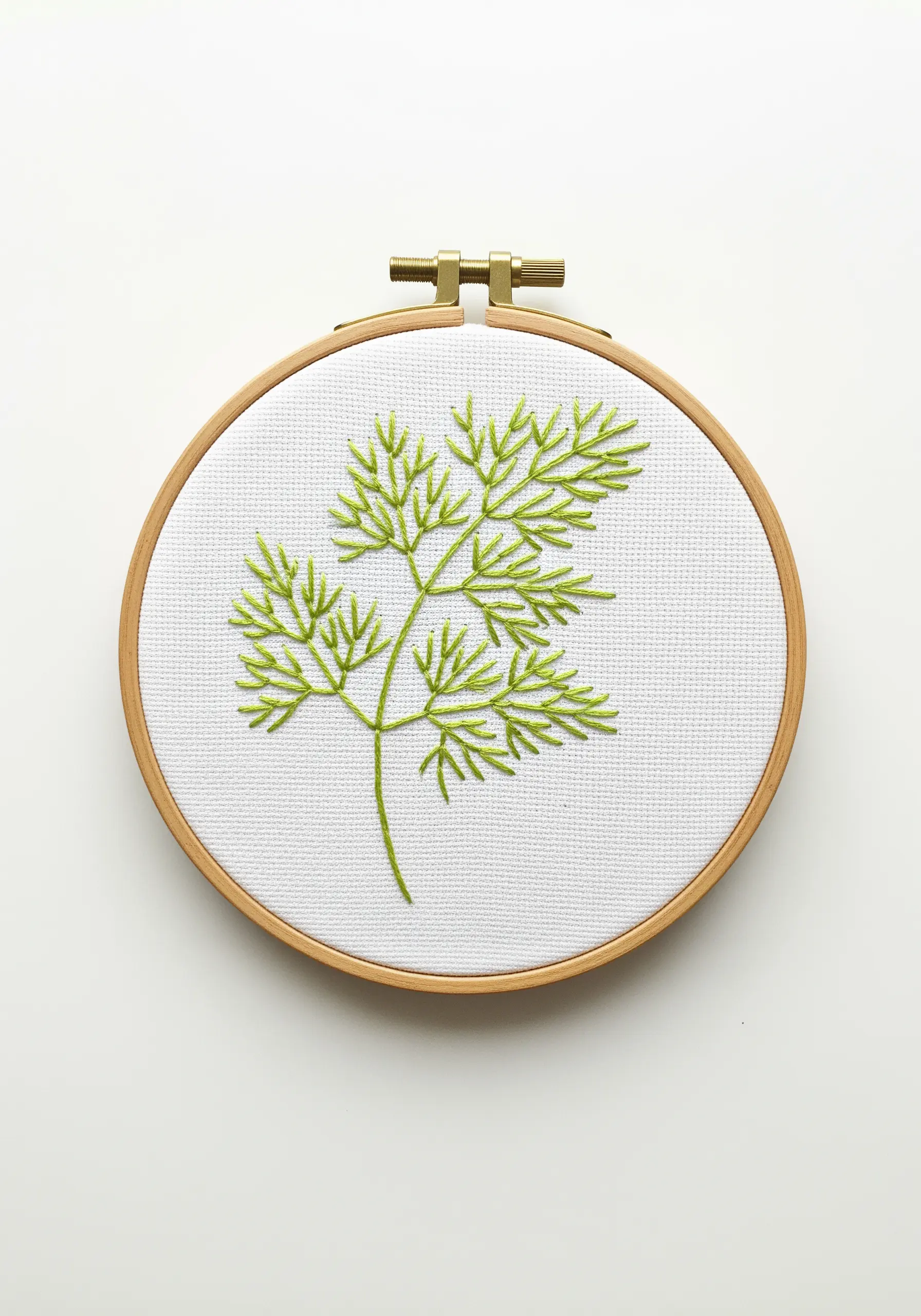 A delicate sprig of dill embroidered with fine, light green straight stitches on white Aida cloth.