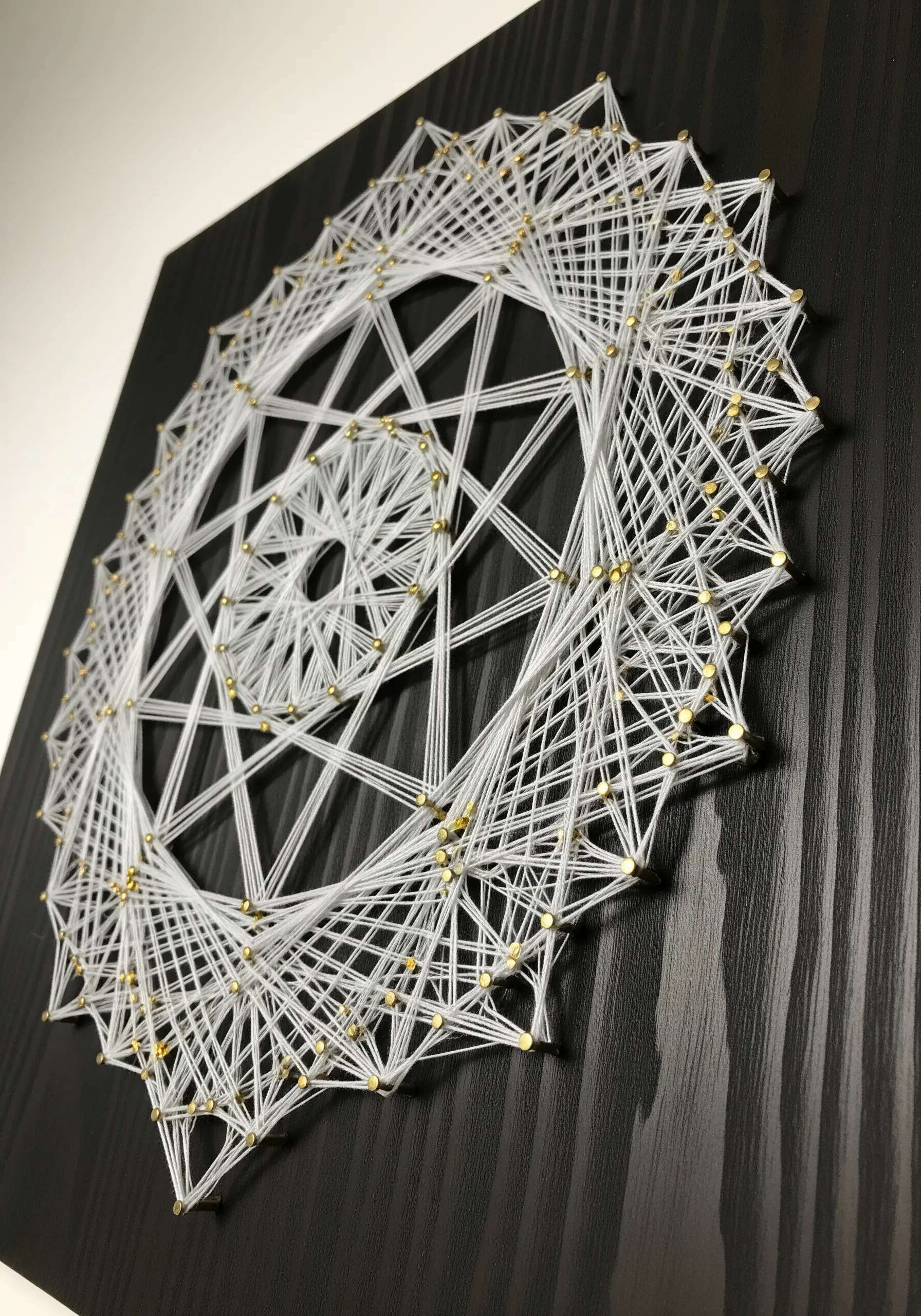 Intricate geometric string art mandala made with white thread on a black wooden board.