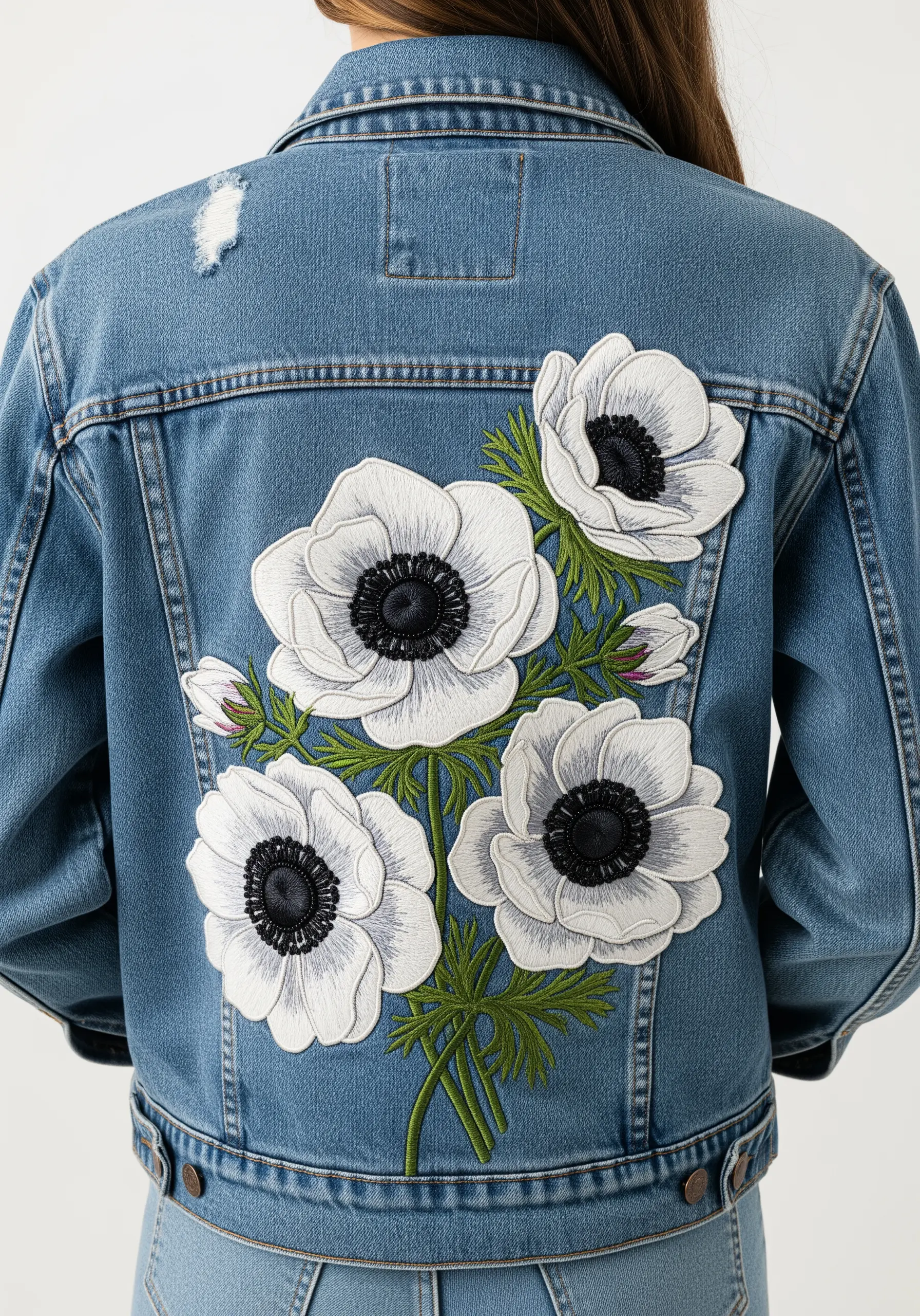 White floral embroidery on the back of a blue denim jacket