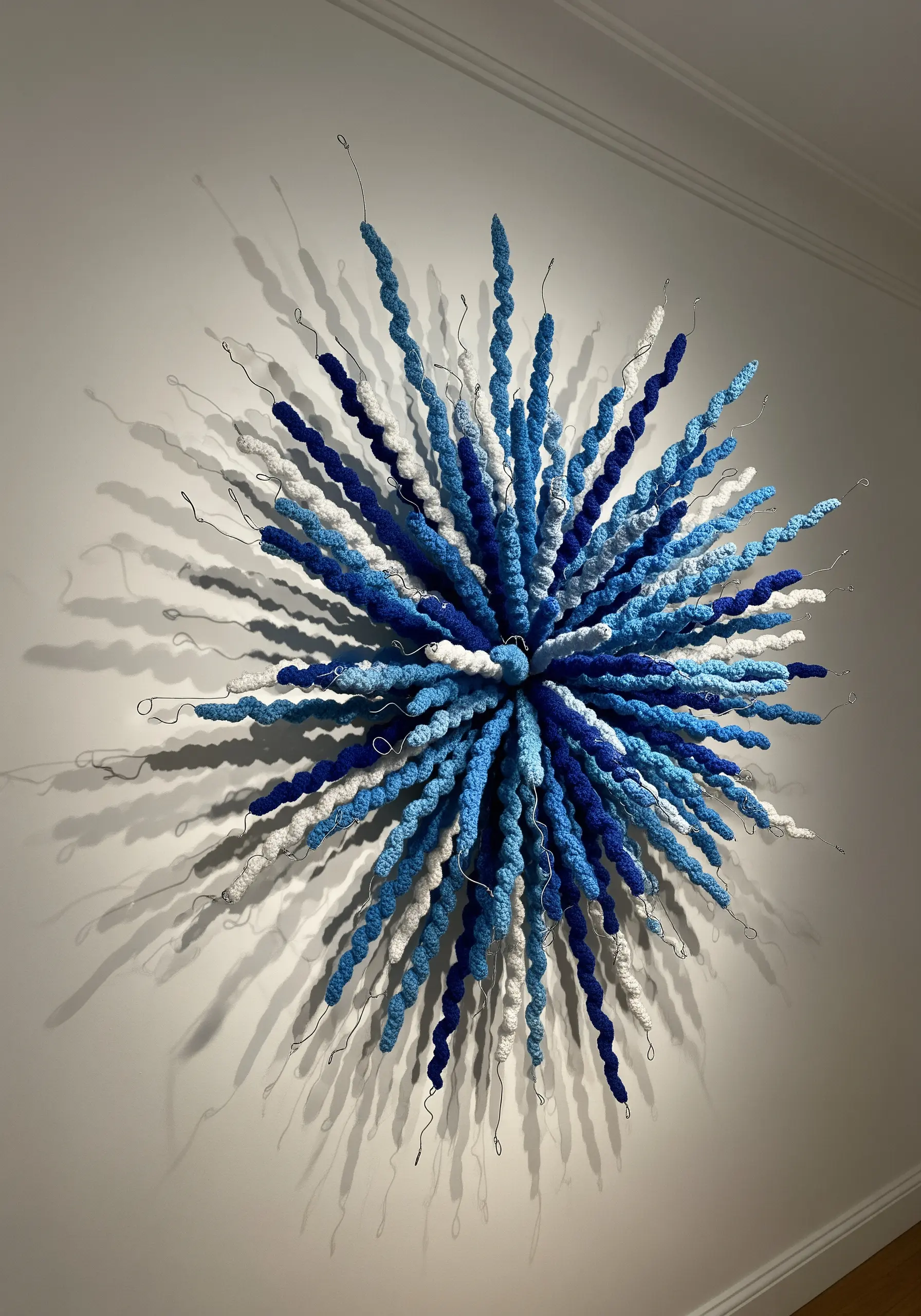 A 3D wall sculpture with blue and white yarn-wrapped wires bursting from a central point.