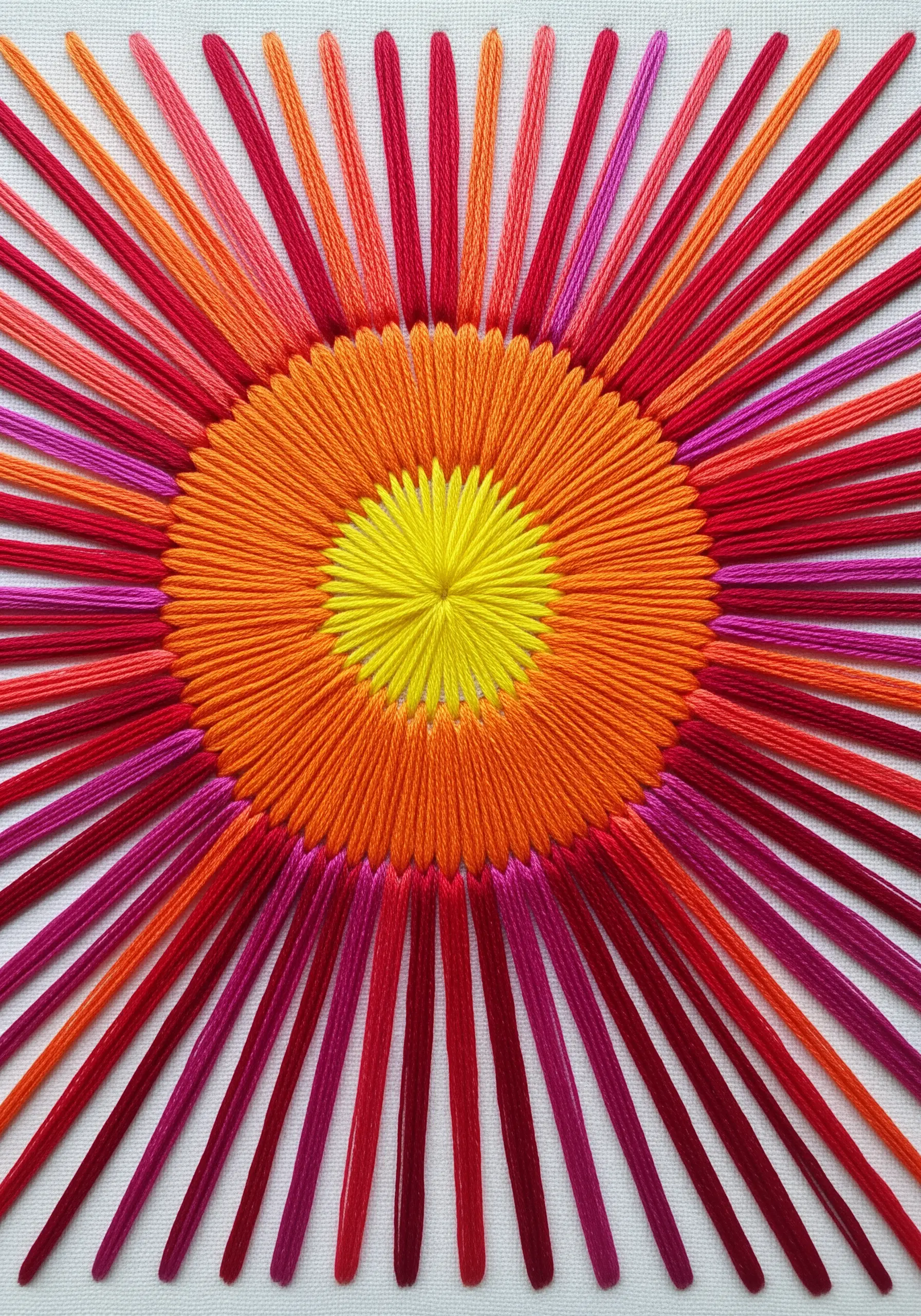 A bold, graphic sunburst with satin stitch and radiating straight stitches in warm colors.