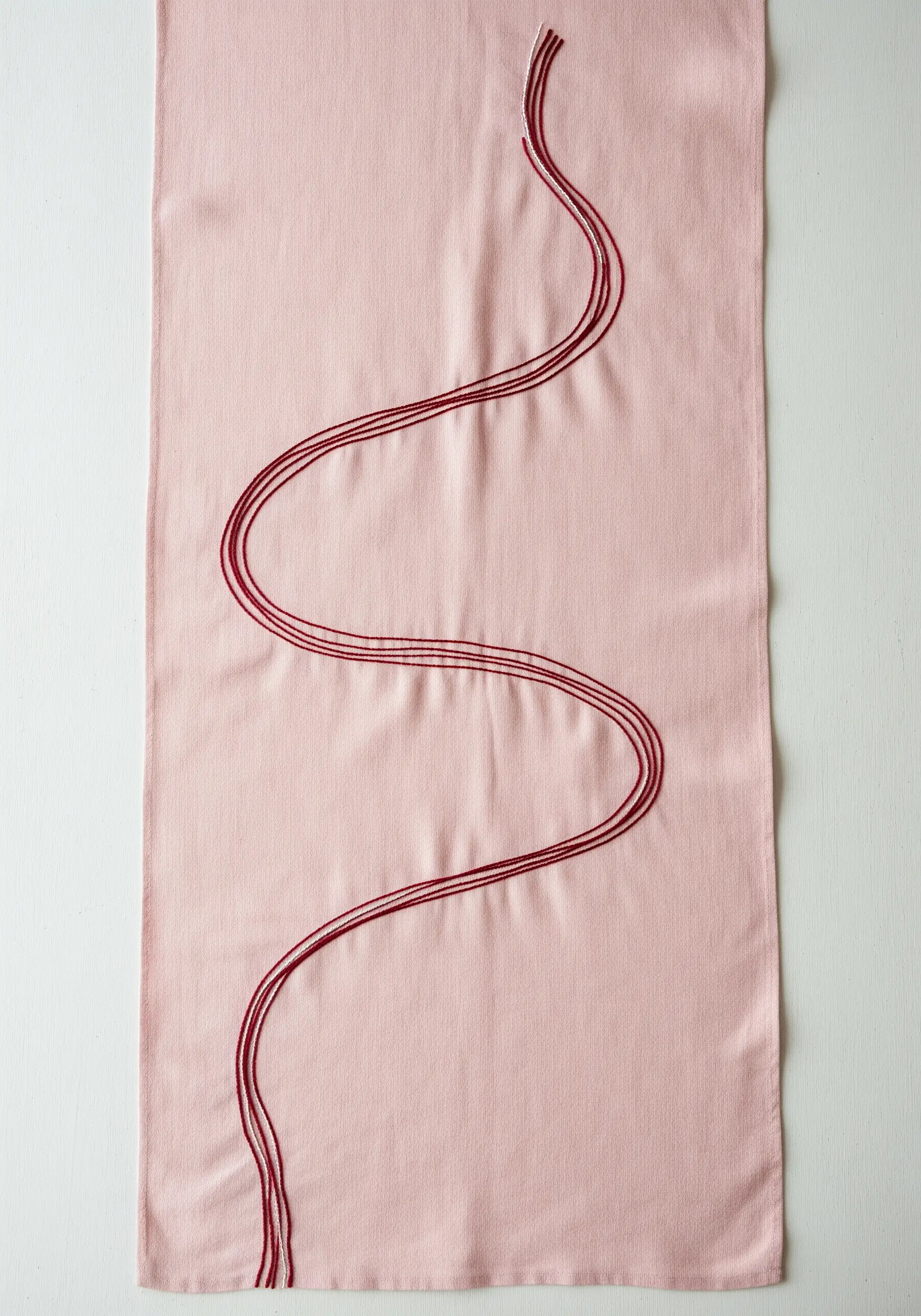 A long, flowing wave pattern stitched with tonal red threads on a pink table runner.