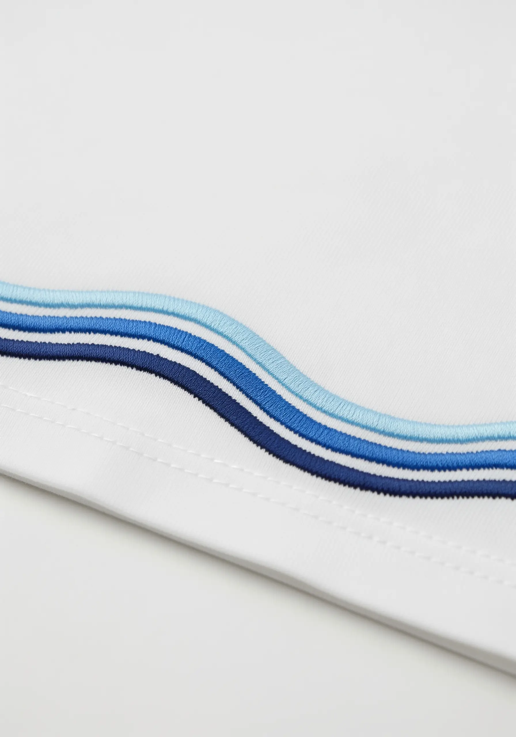 Three parallel wavy lines in shades of blue embroidered on a t-shirt hem.