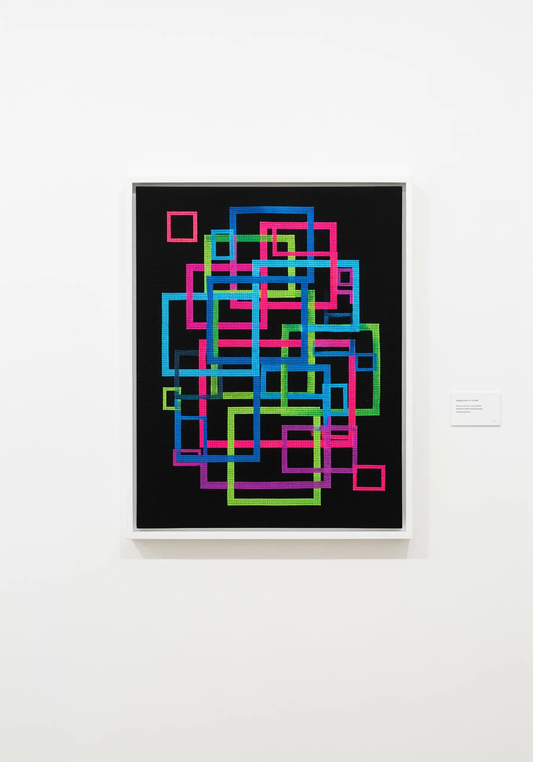 Neon geometric squares cross-stitched on black fabric and framed.
