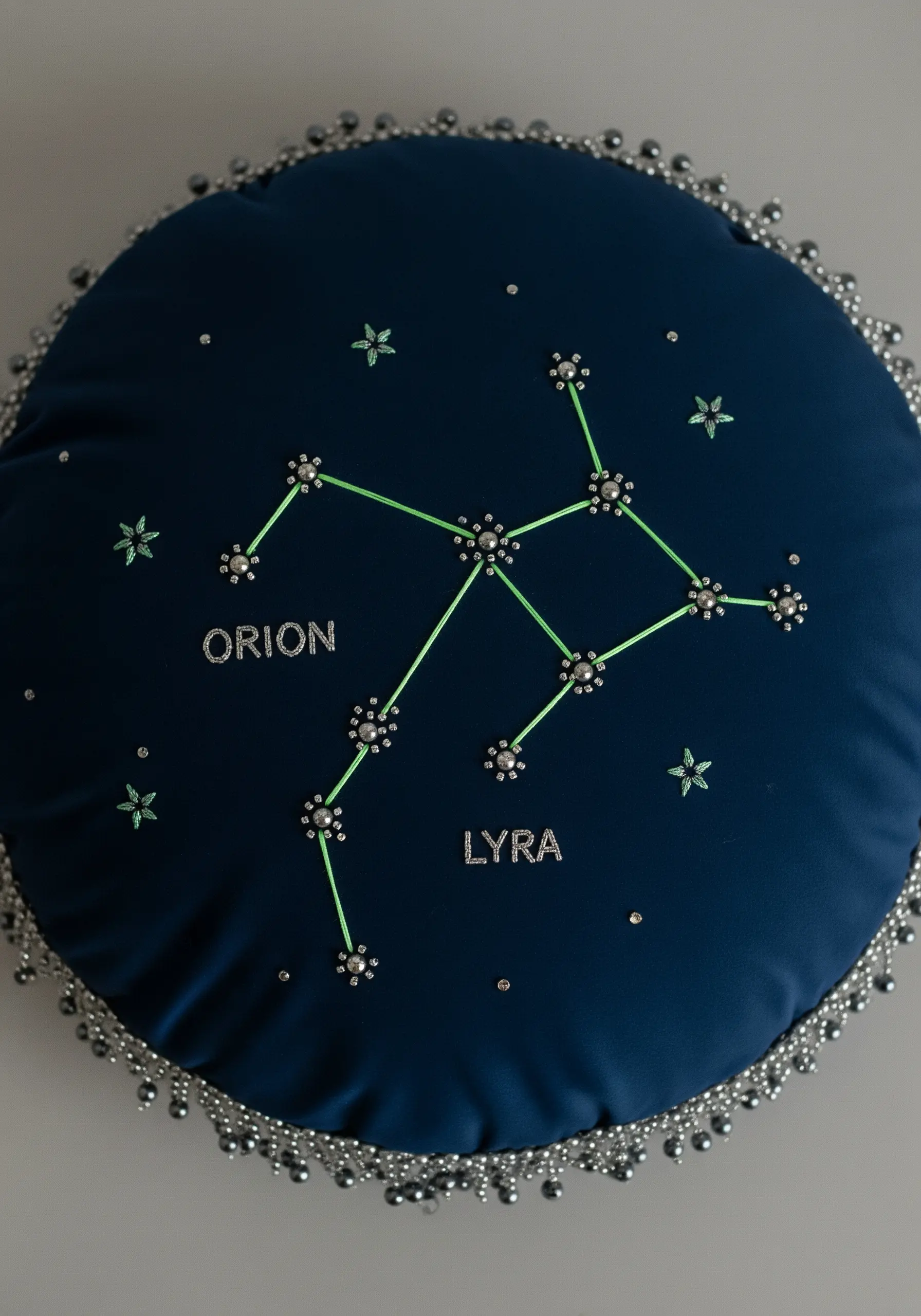 Embroidered constellation patterns on a dark blue pillow, using beads for stars.