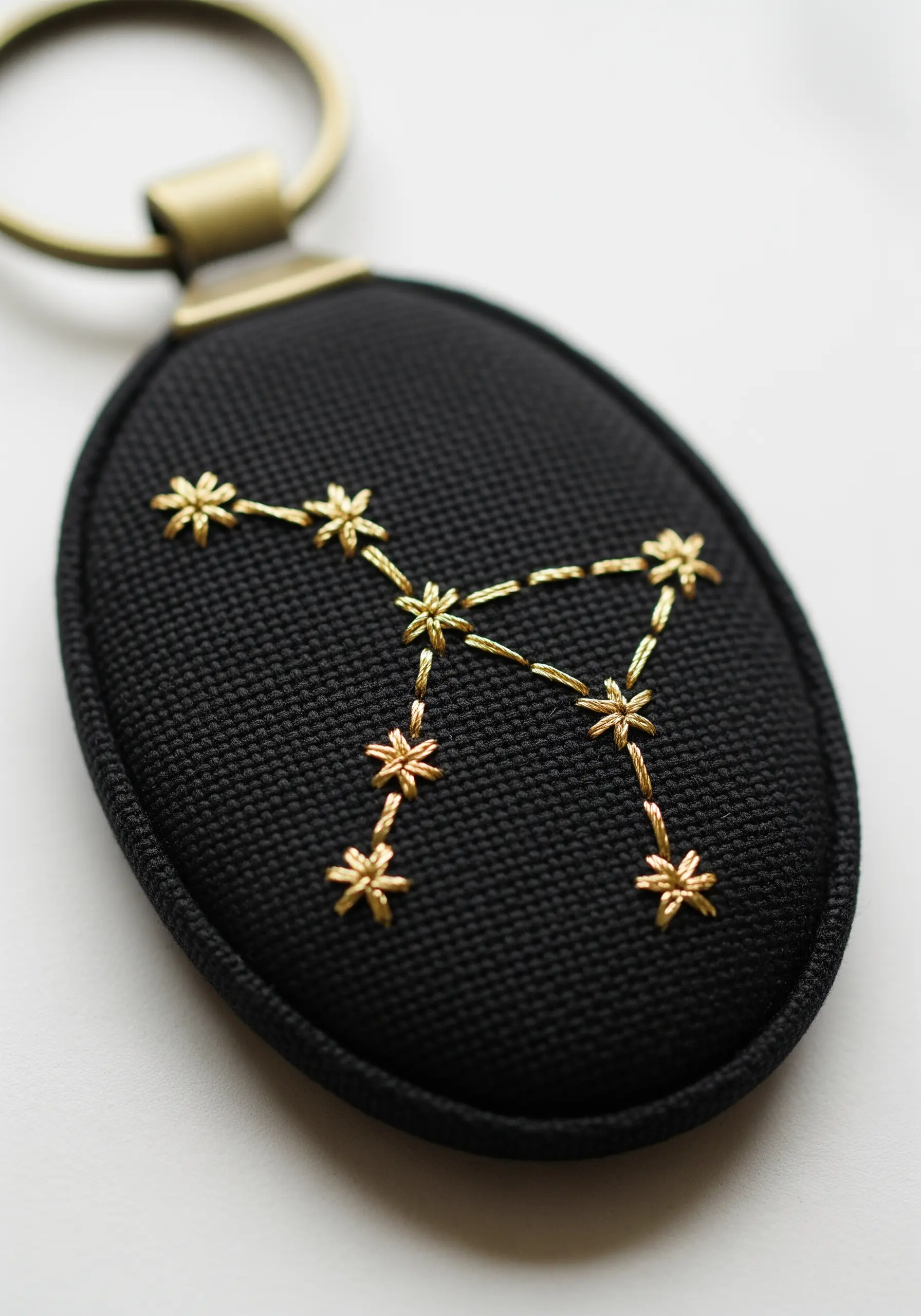 Gold metallic thread constellation embroidered on a black oval keychain