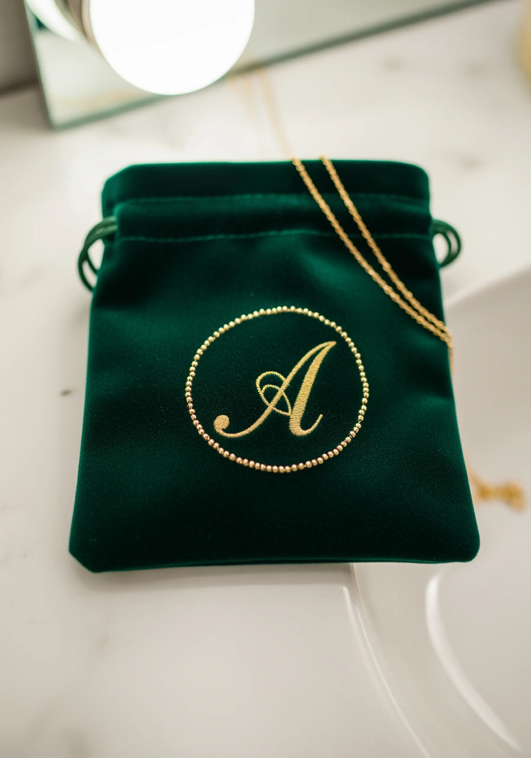 A gold-embroidered 'A' monogram on a dark green velvet jewelry pouch.
