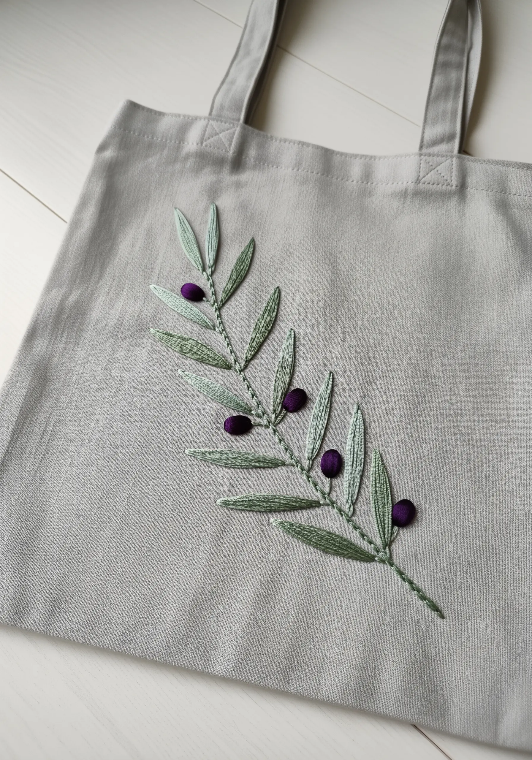 Minimalist olive branch embroidery with 3D padded satin stitch olives on a grey tote.