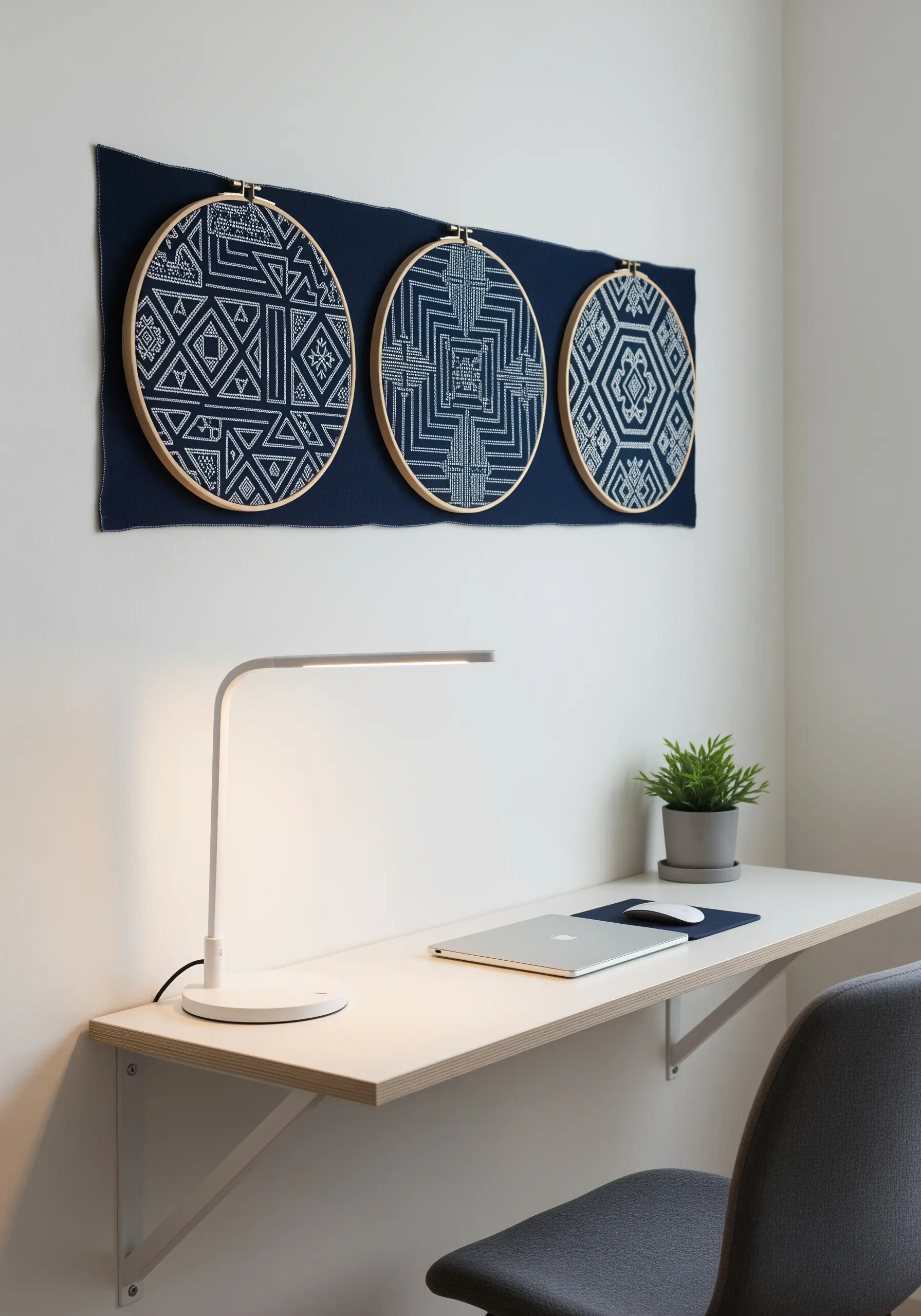 Three blue and white geometric embroidery hoops mounted on a dark navy fabric panel over a desk.