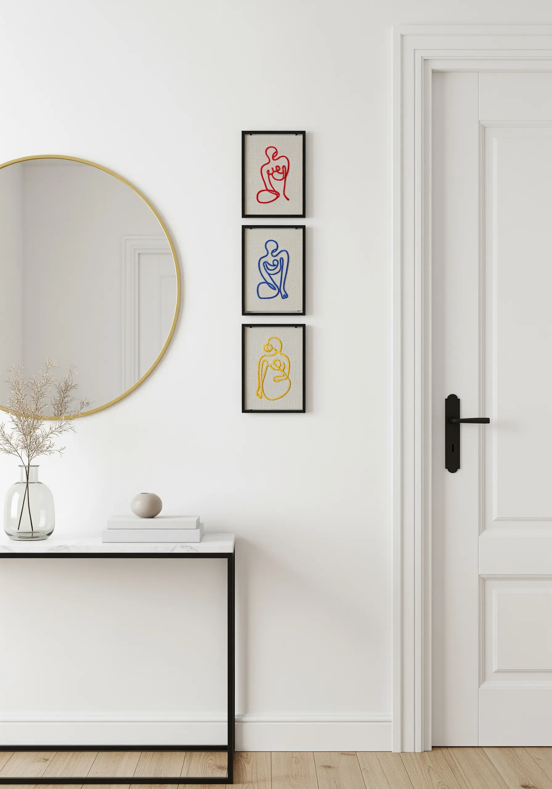 A set of three small framed line-art embroideries of figures in red, blue, and yellow.