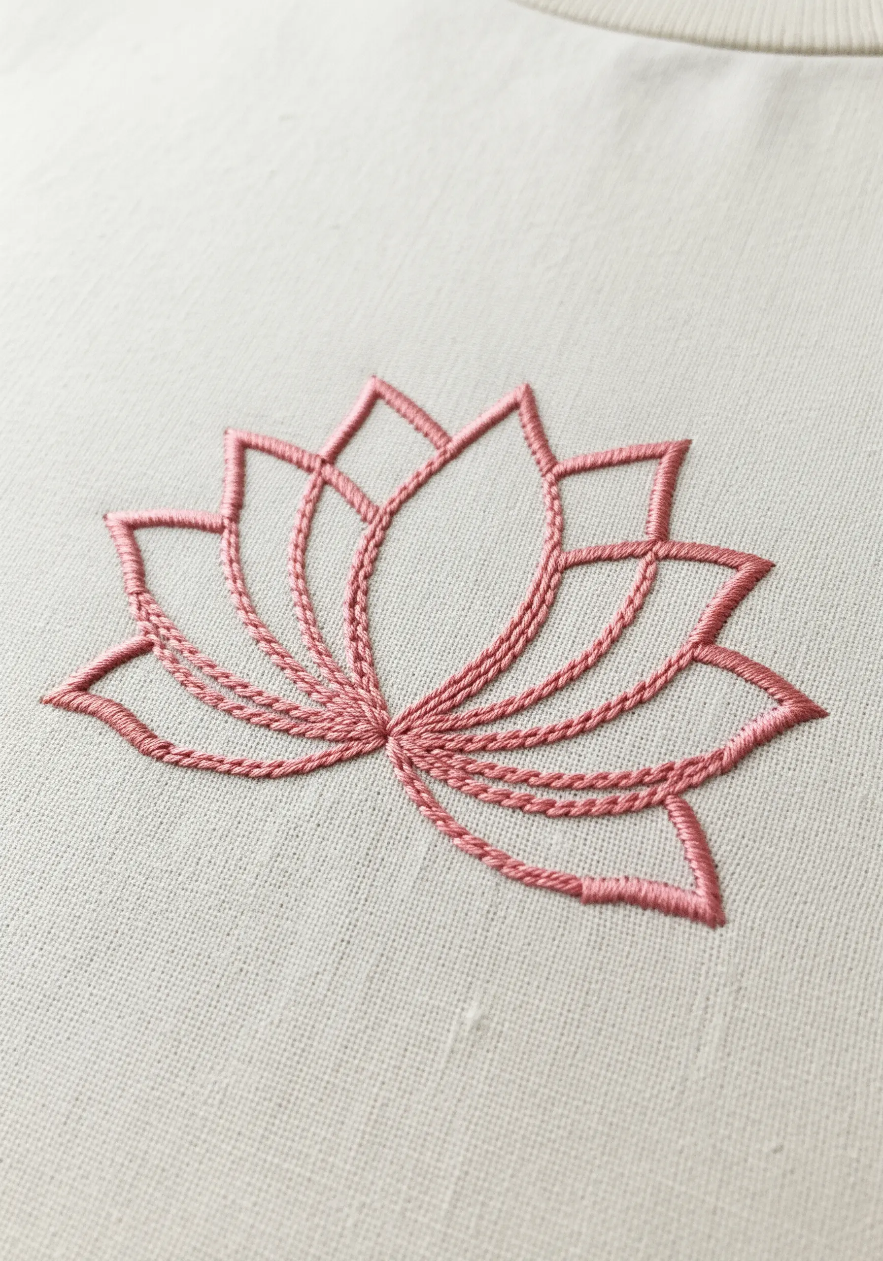 A pink lotus flower outline made with whipped chain stitch on cream fabric.