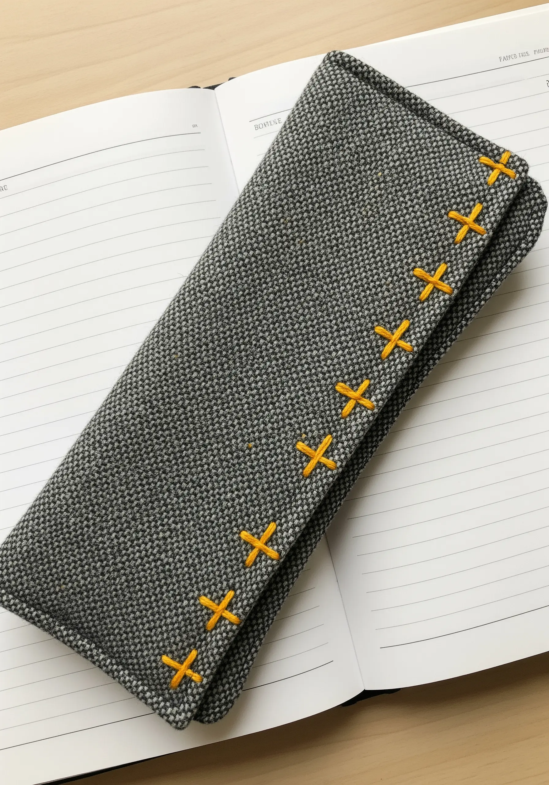 A gray tweed glasses case with a decorative closure of bright yellow cross-stitches.