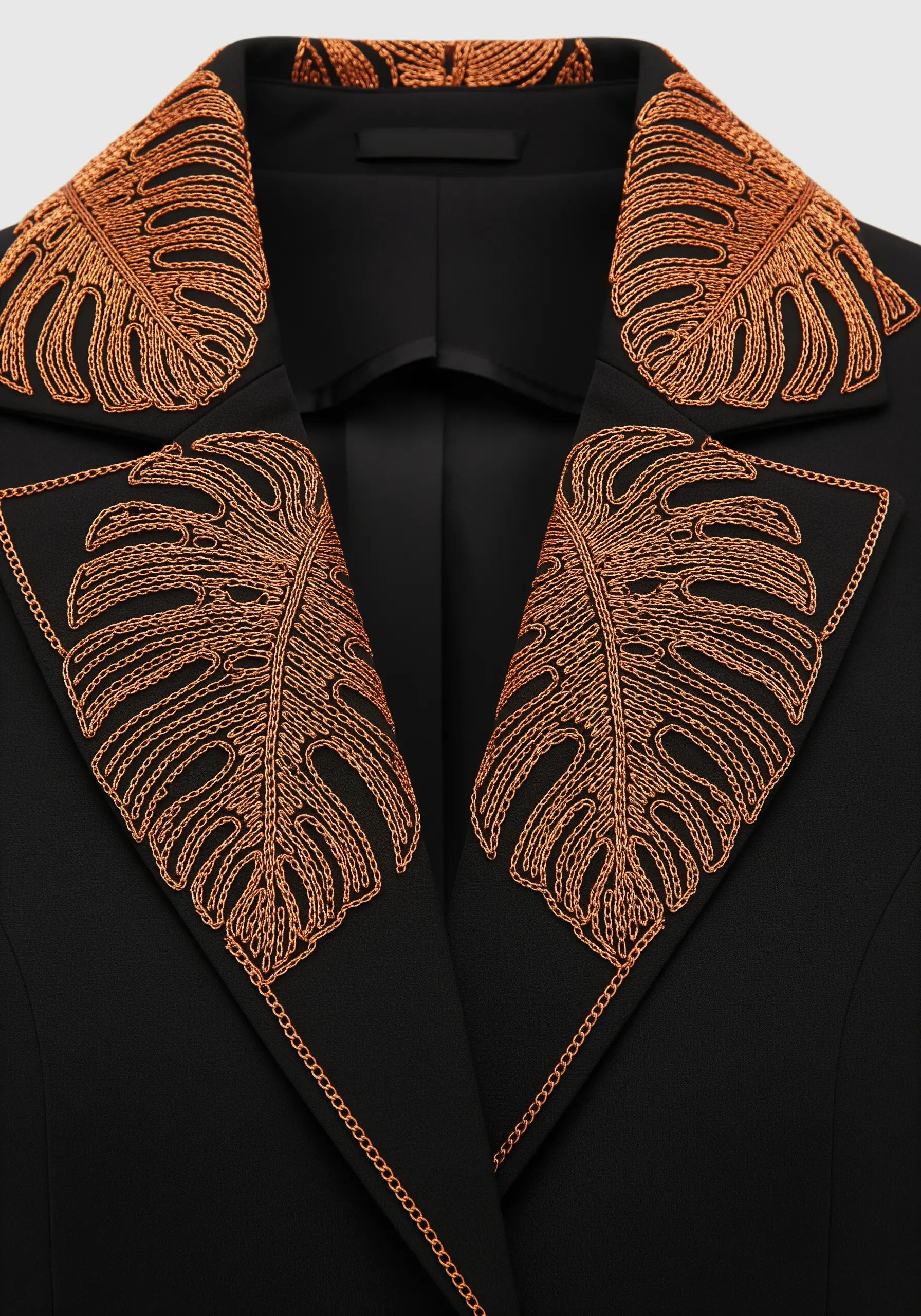 Copper metallic thread embroidery of monstera leaves on the lapels of a black blazer.