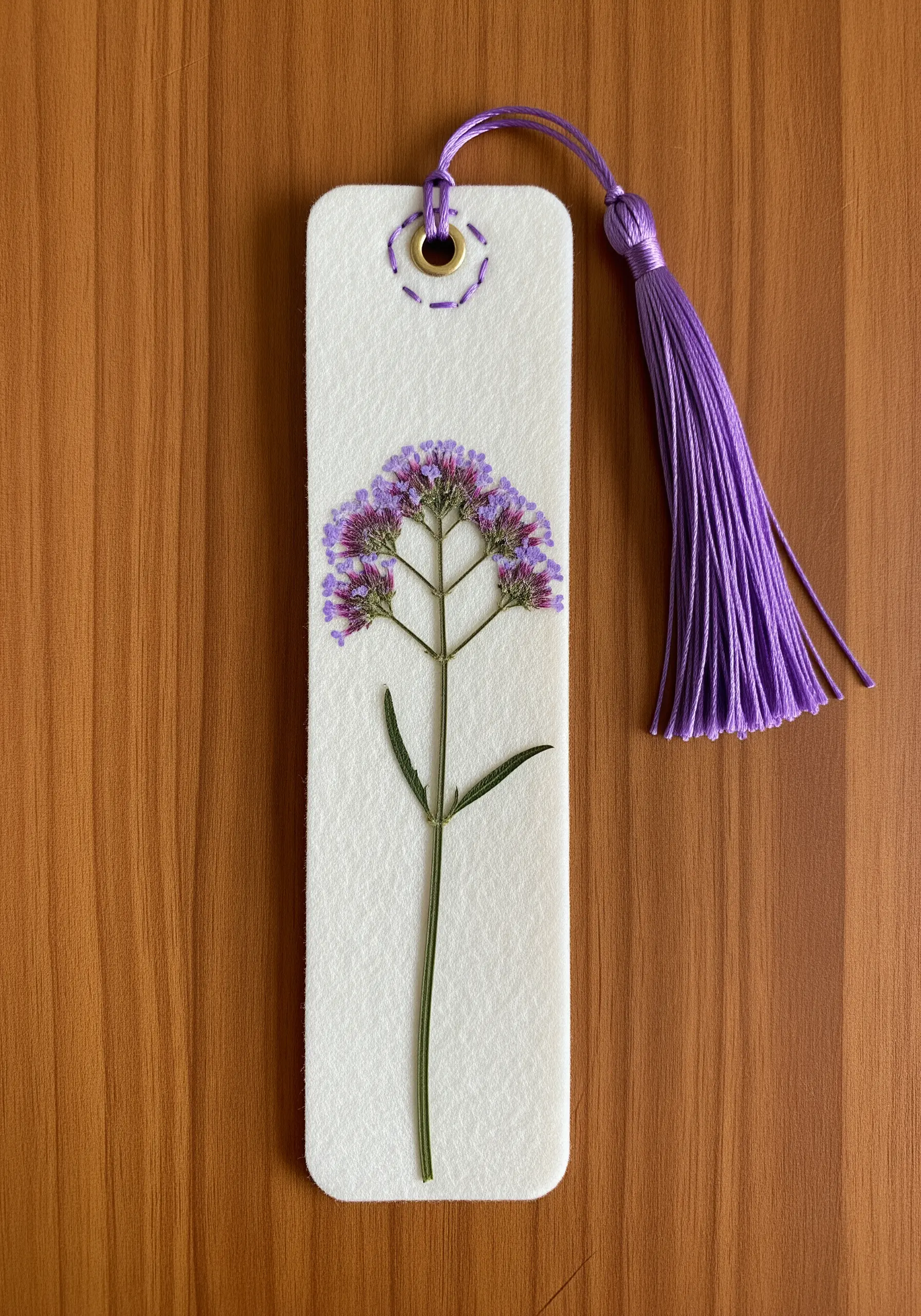 A pressed verbena flower on a white felt bookmark with a purple tassel.