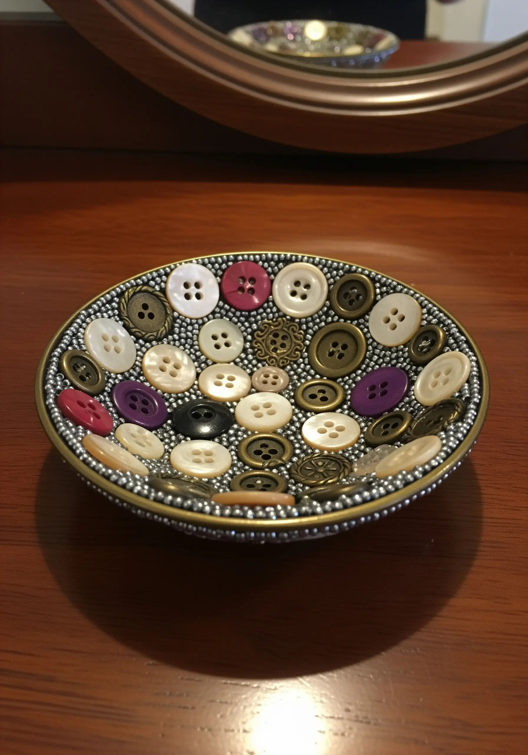A small decorative bowl lined with a mosaic of colorful and metallic buttons.