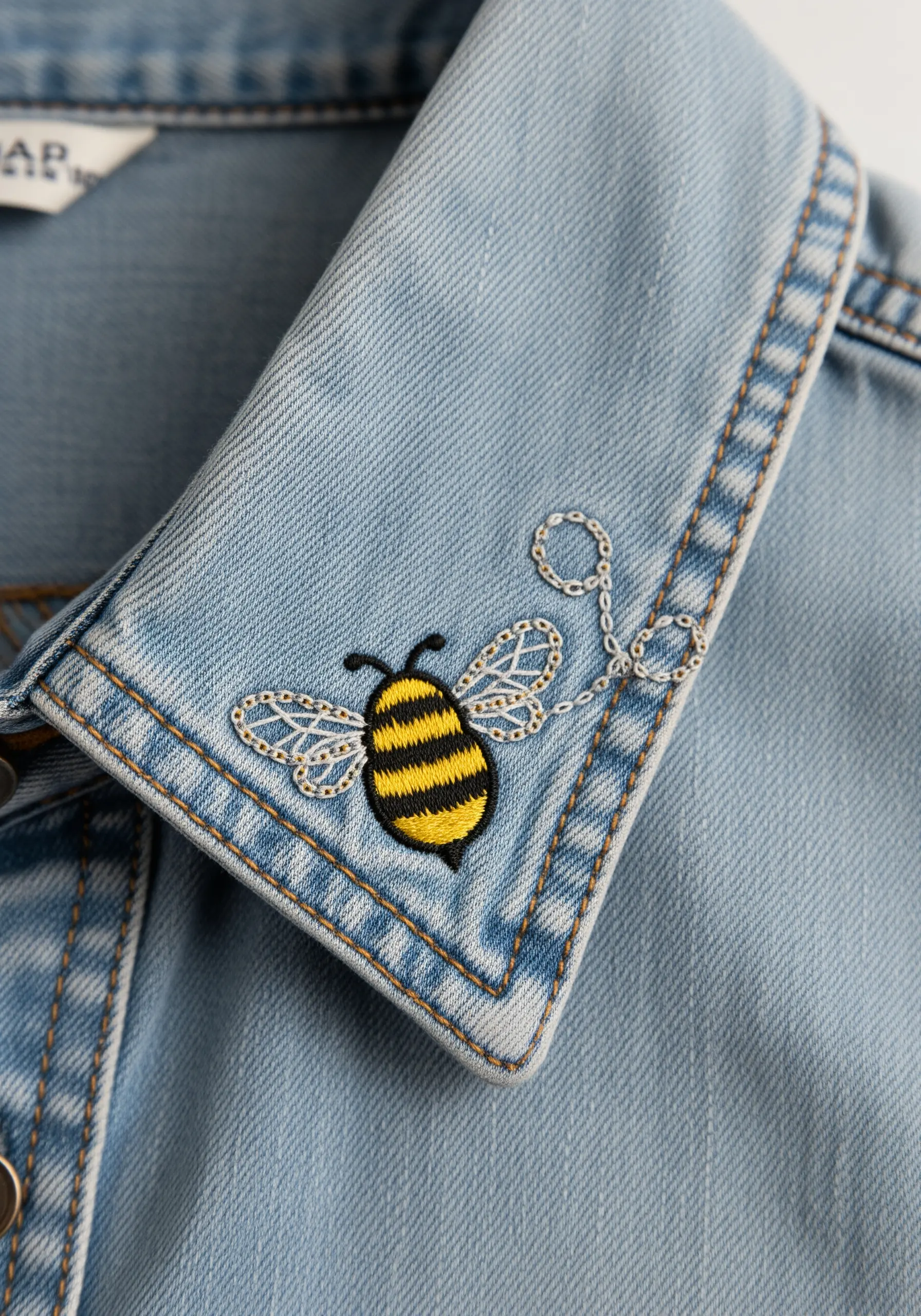 A tiny embroidered bee with delicate wings on the collar of a denim jacket.