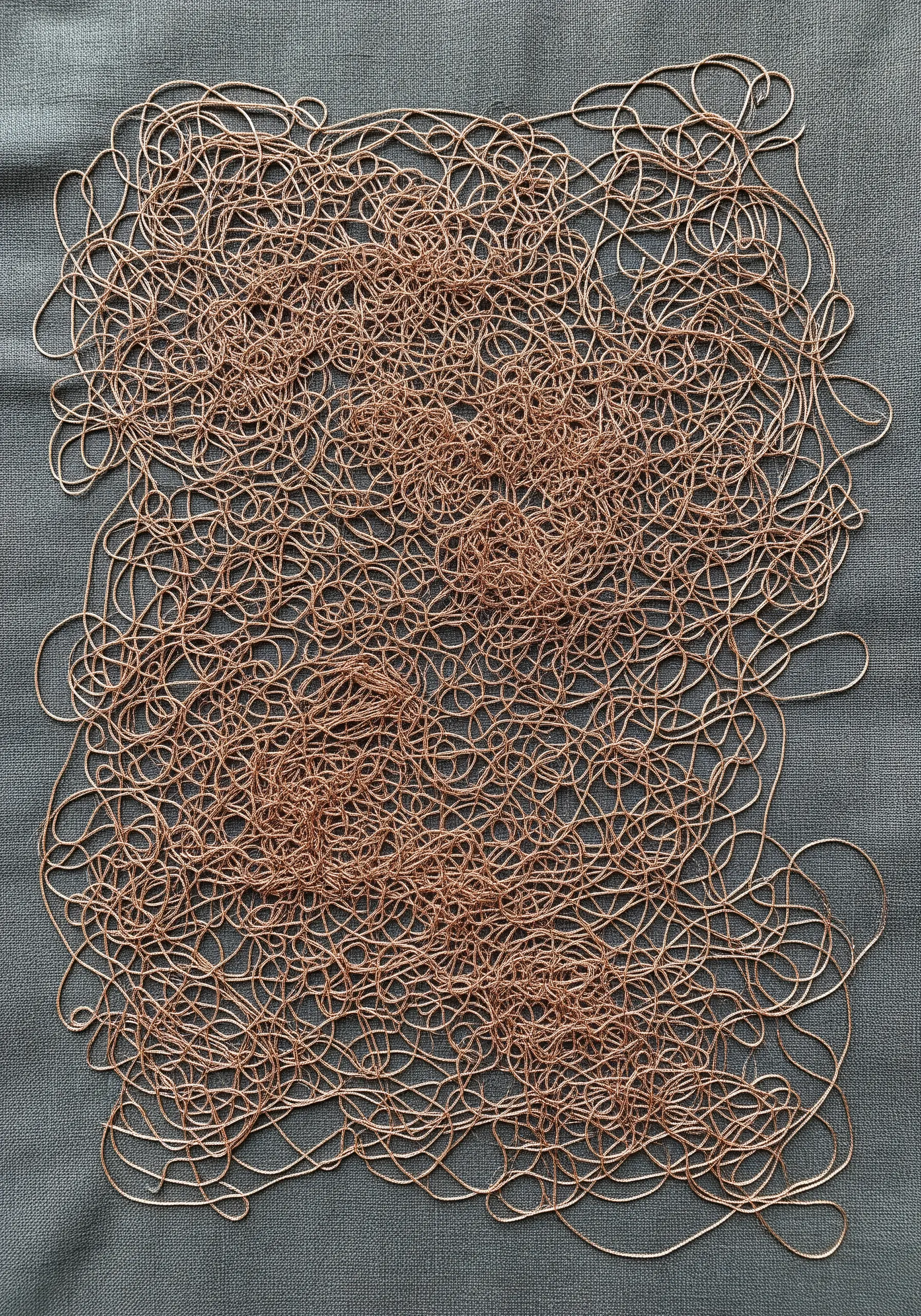 A chaotic, tangled web of copper metallic thread stitched onto a grey fabric background.