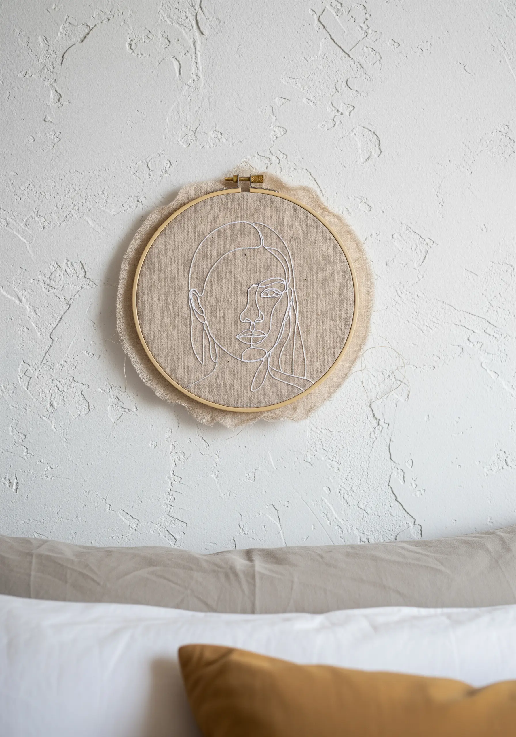 An embroidery hoop with a white line art portrait, with the raw, untrimmed fabric left visible.