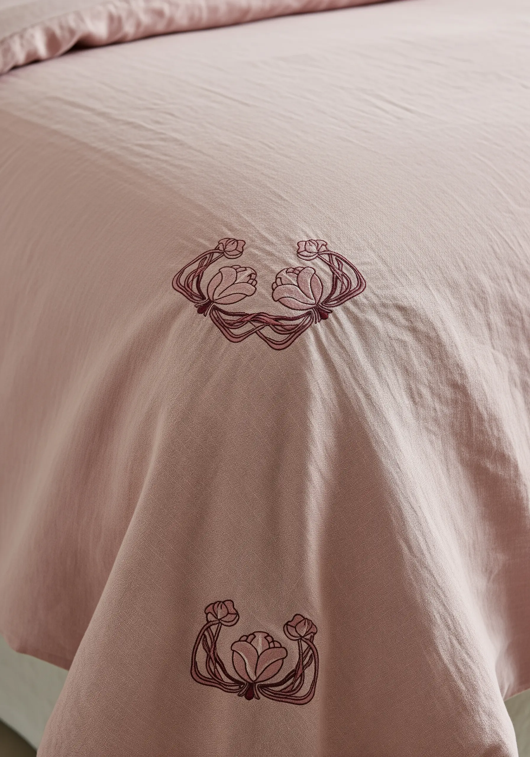 Tonal Art Nouveau floral motifs embroidered in a swirling pattern on a dusty pink duvet cover.